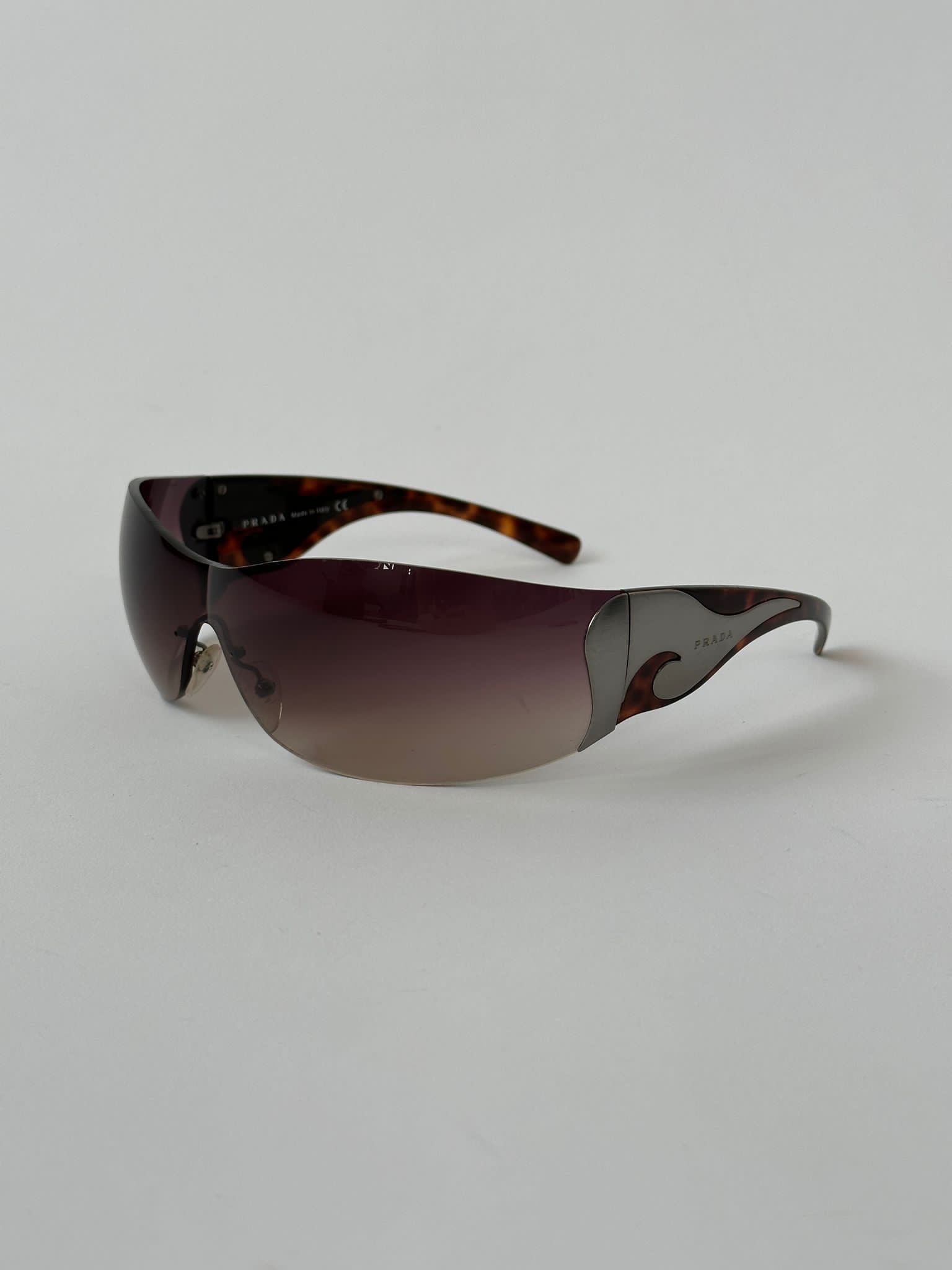 Prada Flame Rimless Wrap Sunglasses with sleek, modern design and transparent lenses, showcasing a stylish eyewear accessory.