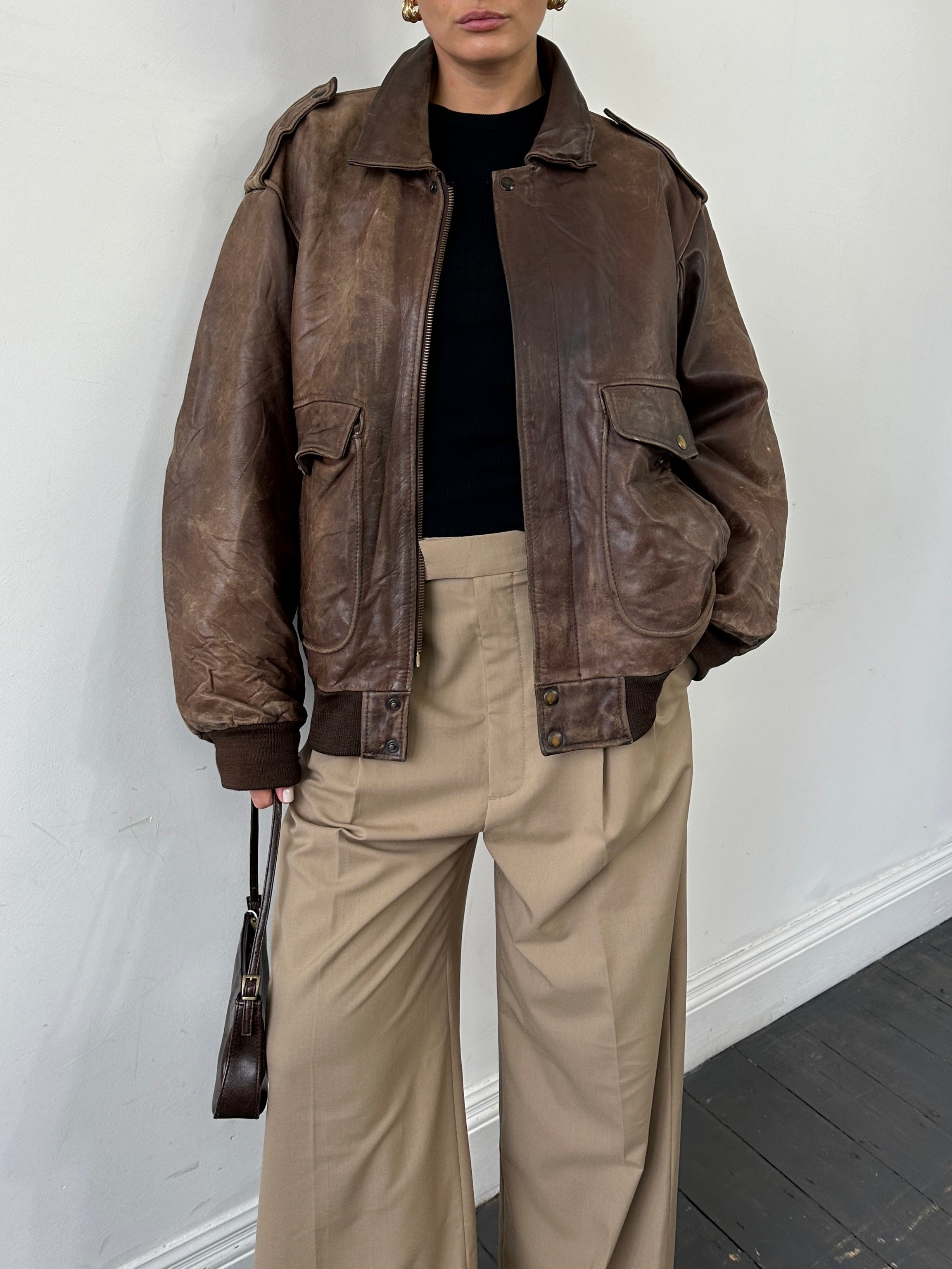 Vintage distressed leather bomber jacket in XL size, featuring worn detailing and classic style, displayed on a hanger.