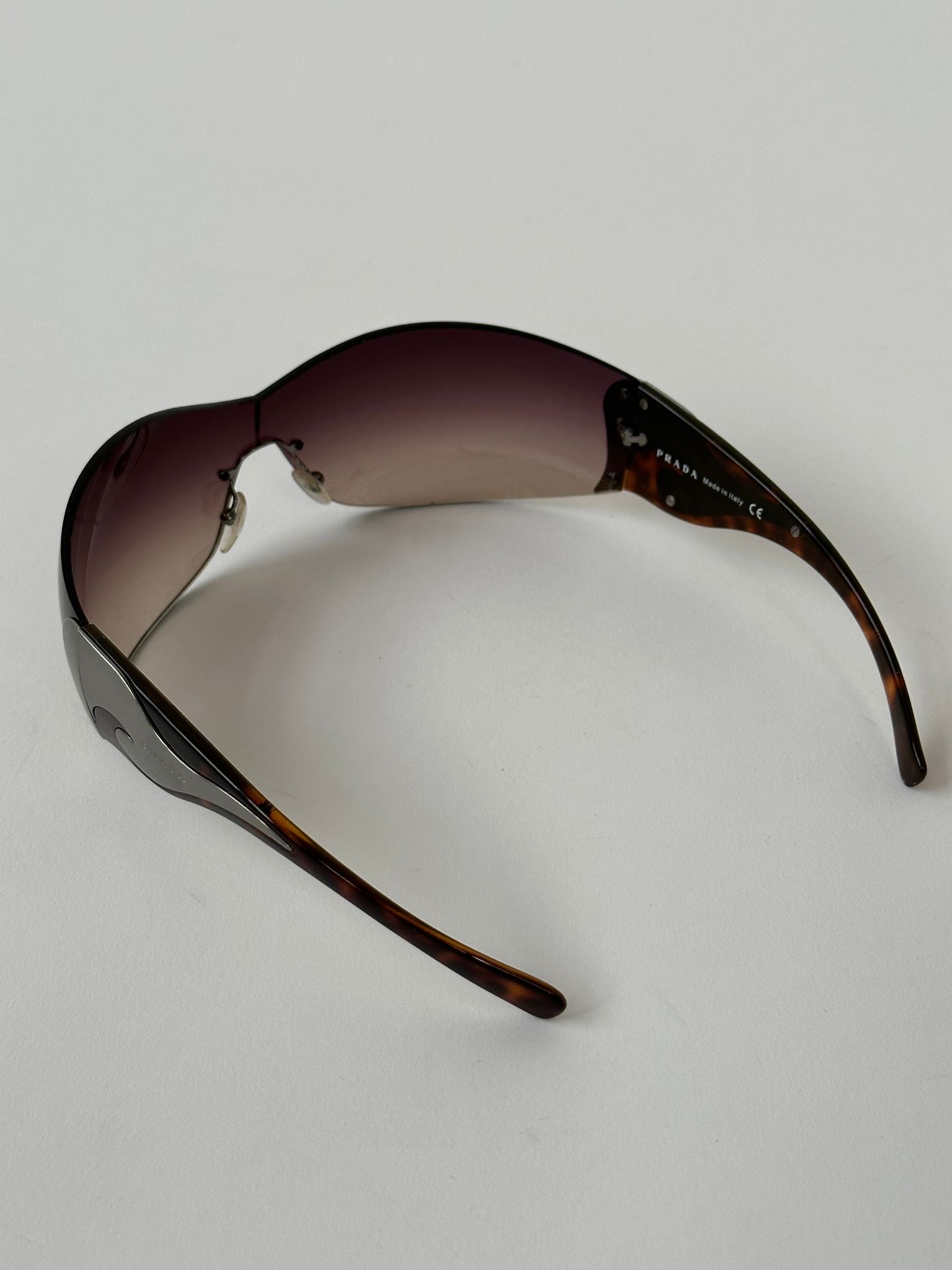 Prada Flame Rimless Wrap Sunglasses with sleek, modern design and dark tinted lenses, featuring a stylish rimless frame.