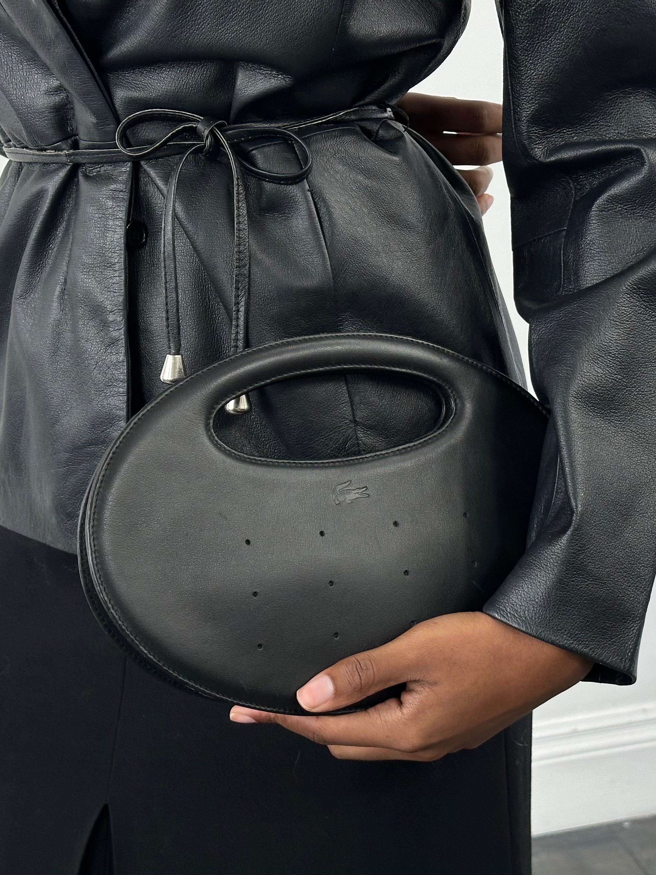 Lacoste 2000s faux leather oval handle bag with sleek design and top zipper closure, featuring Lacoste logo on the front.