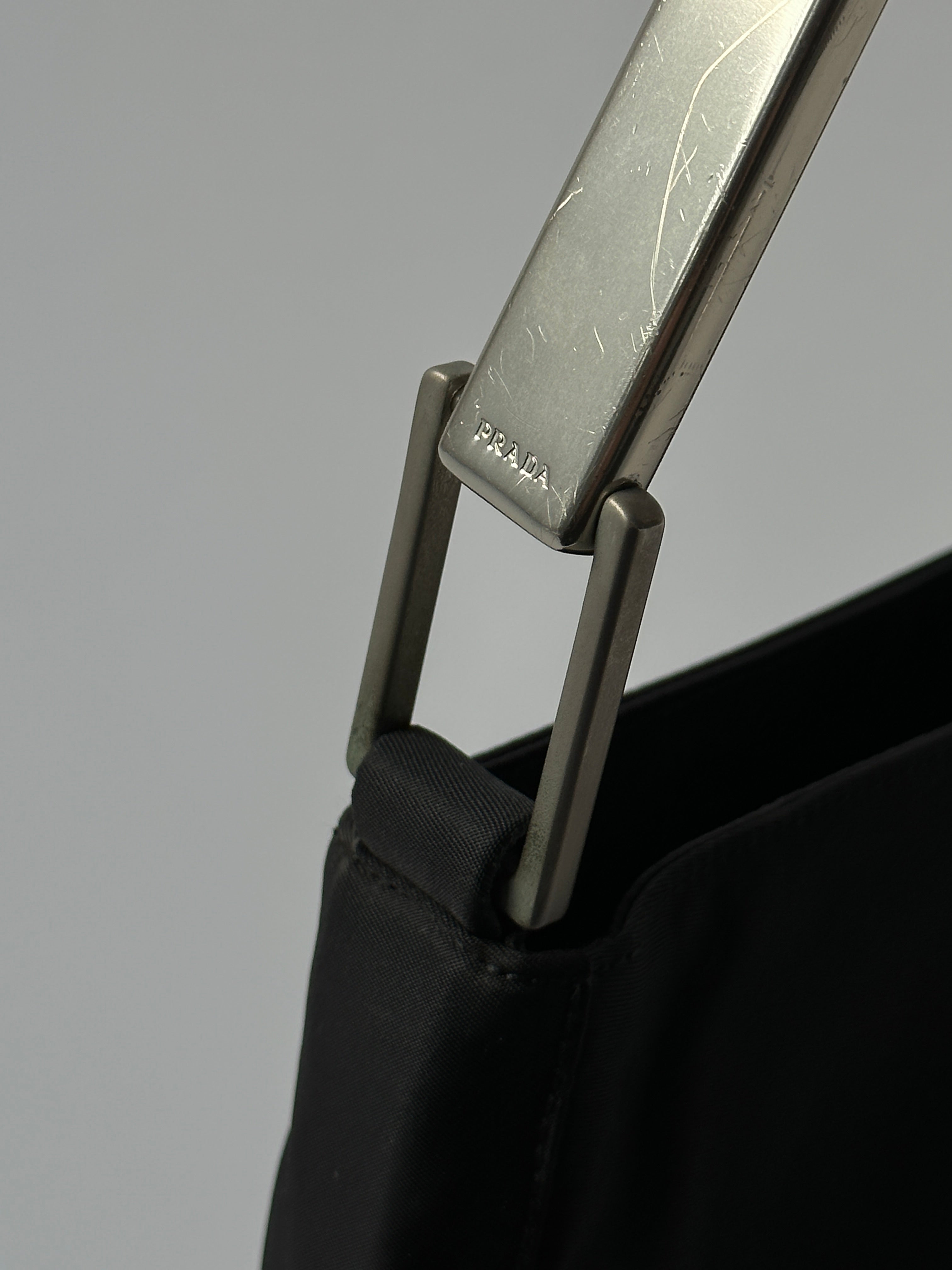Prada nylon shoulder bag with metal handle, featuring sleek design and durable straps.
