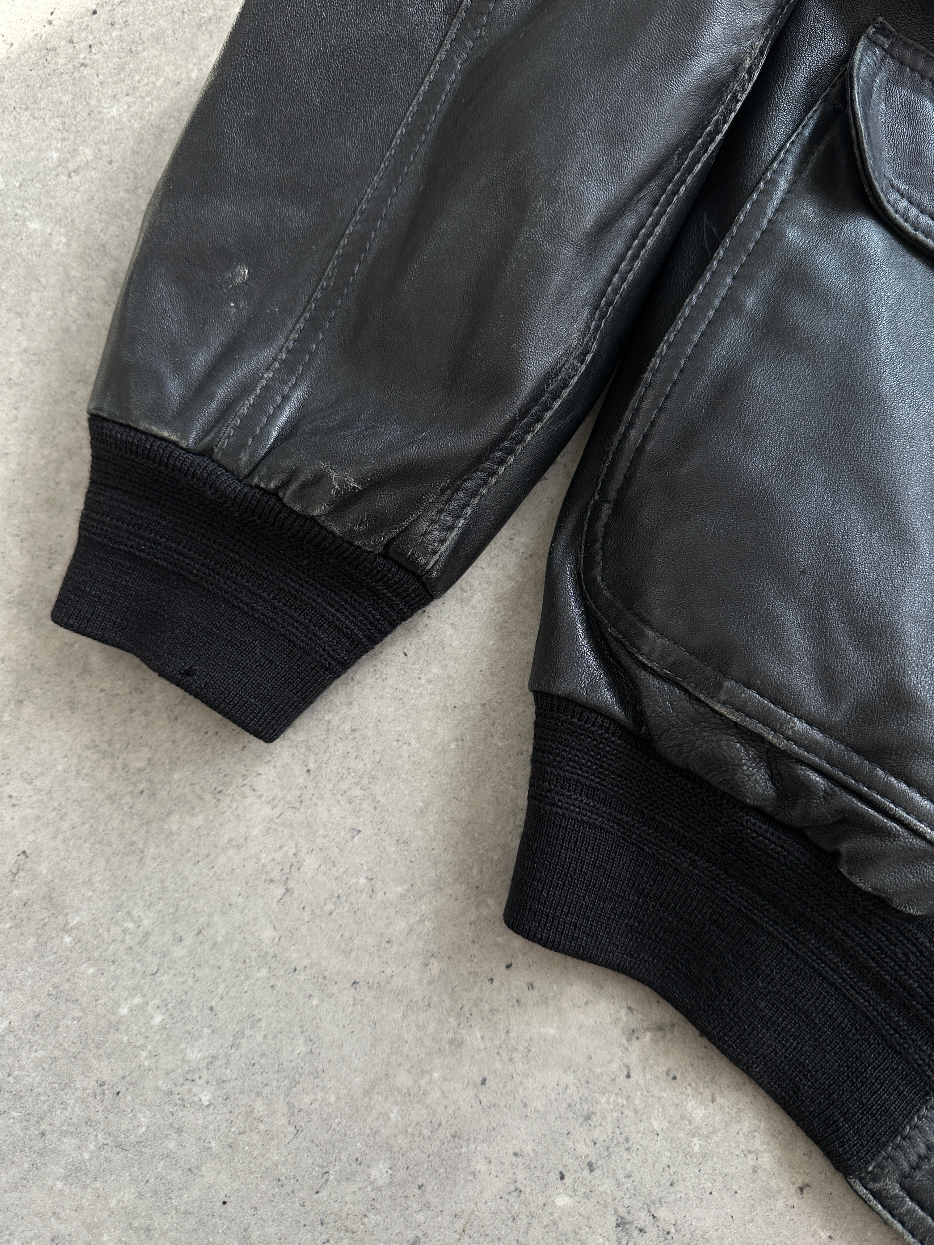 Vintage leather bomber jacket in size M, featuring classic collar, front zipper, and rugged textured leather, displayed on a hanger.