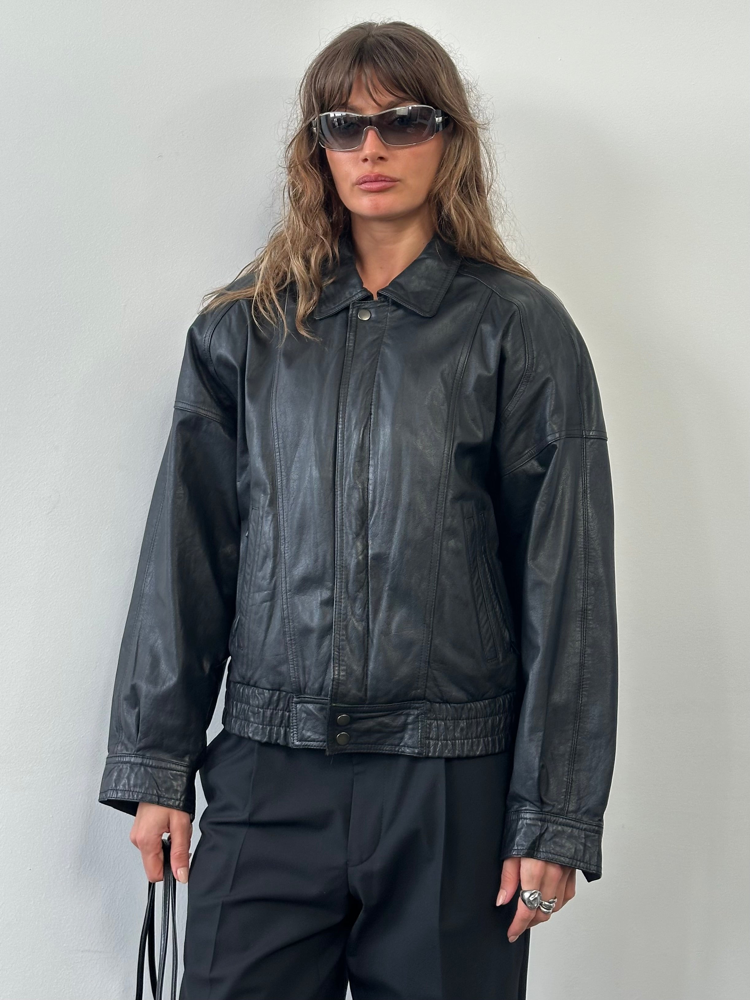 Vintage 1990s leather bomber jacket in medium size with classic design and brown leather exterior, front zipper, and ribbed cuffs.