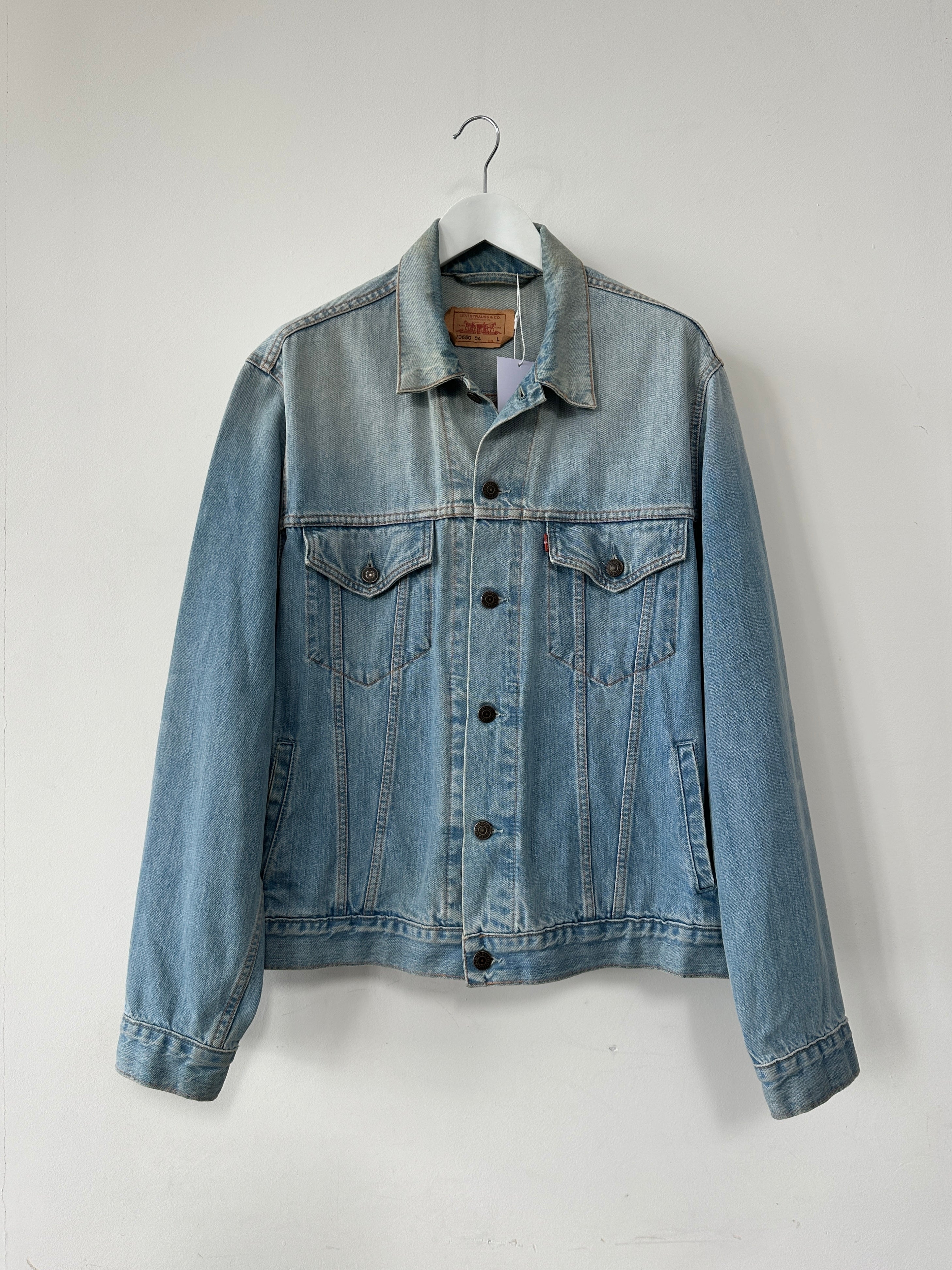 Levi’s faded denim jacket in size L displayed on a hanger with a casual outdoor background.