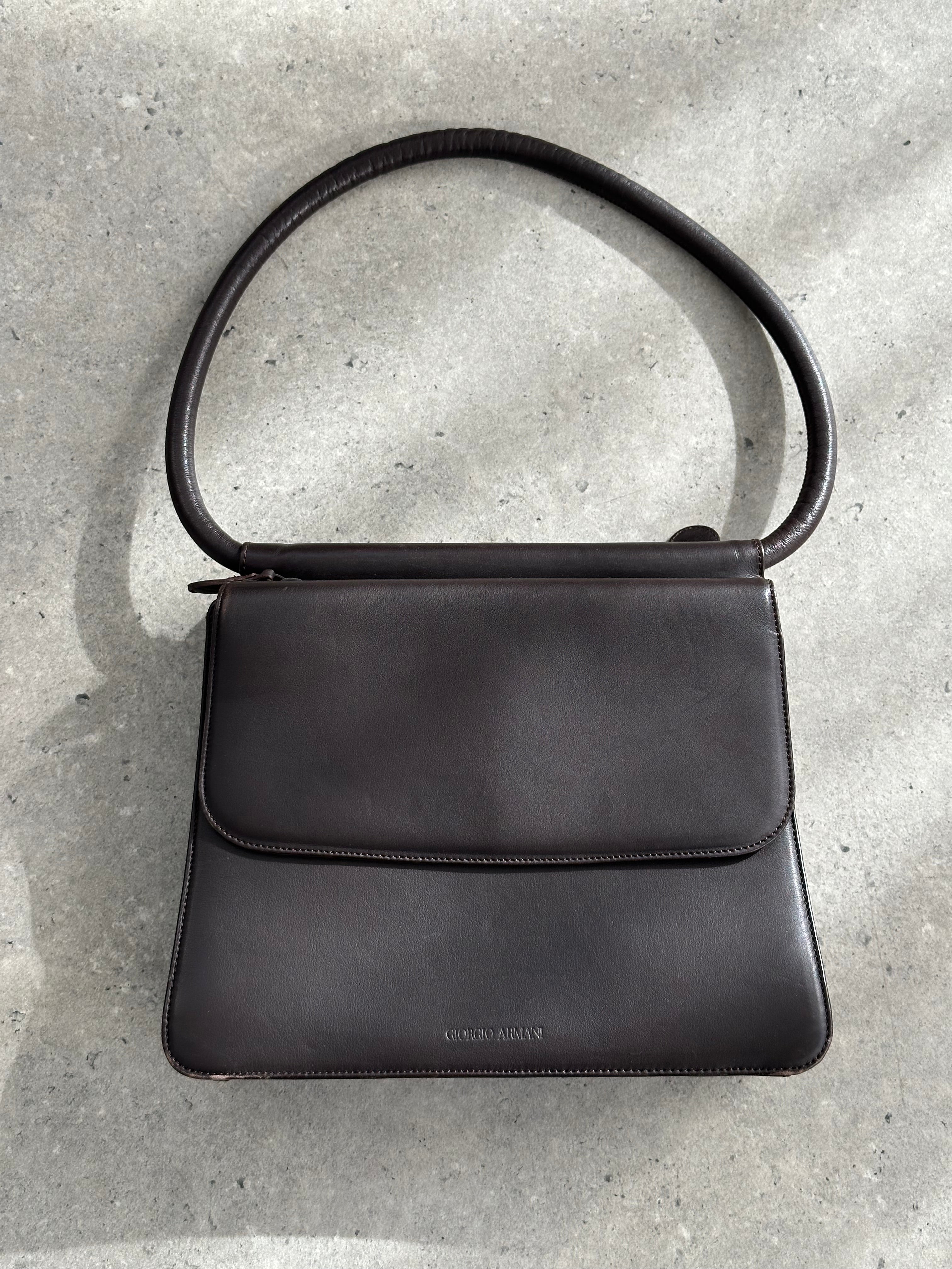 Giorgio Armani Le Collezioni leather shoulder bag with sleek design, top handle, and subtle branding visible in the image.