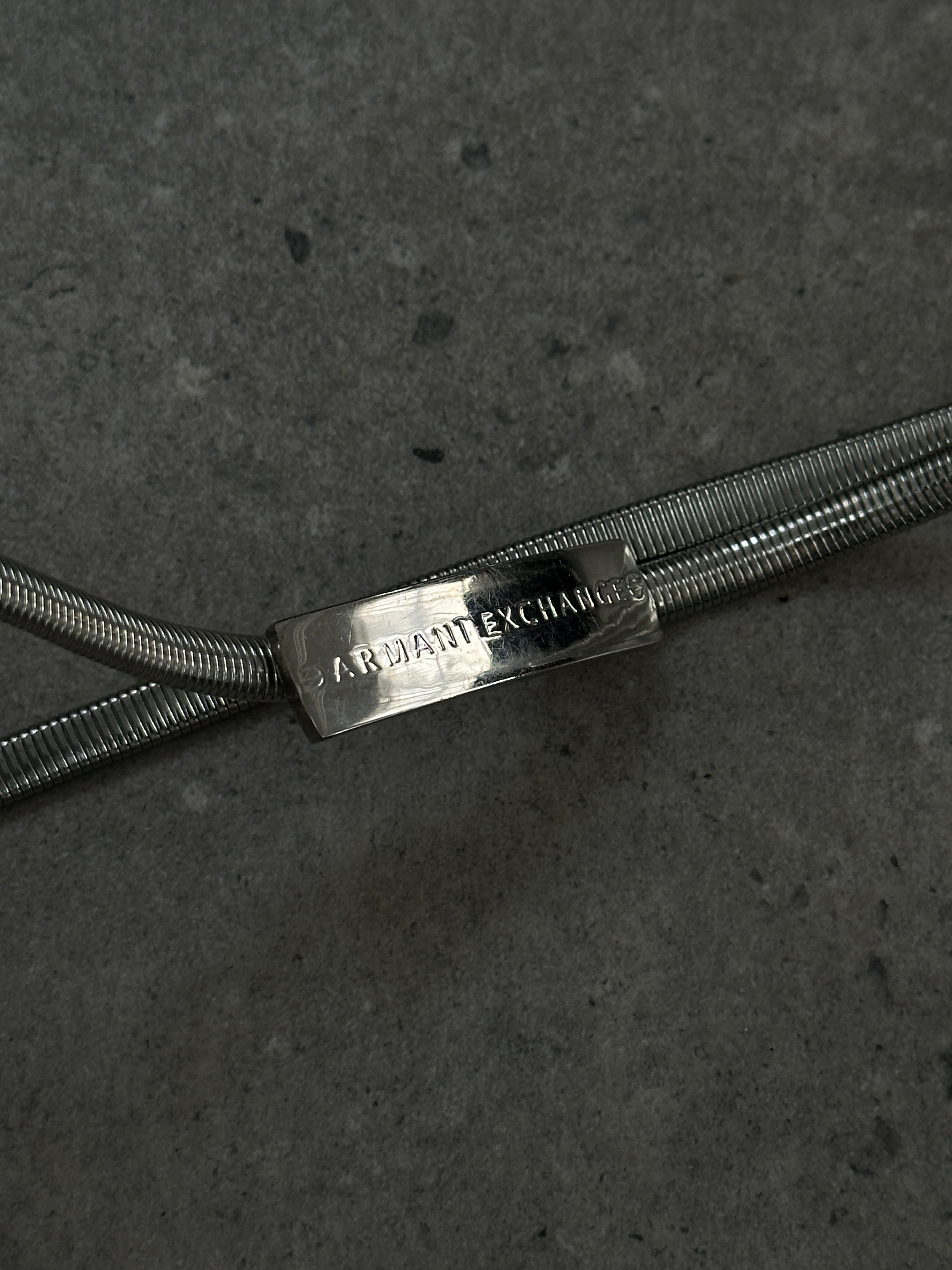 Armani Exchange stretchy metal engraved belt with adjustable 26-30 inch length, featuring a sleek engraved metal buckle.