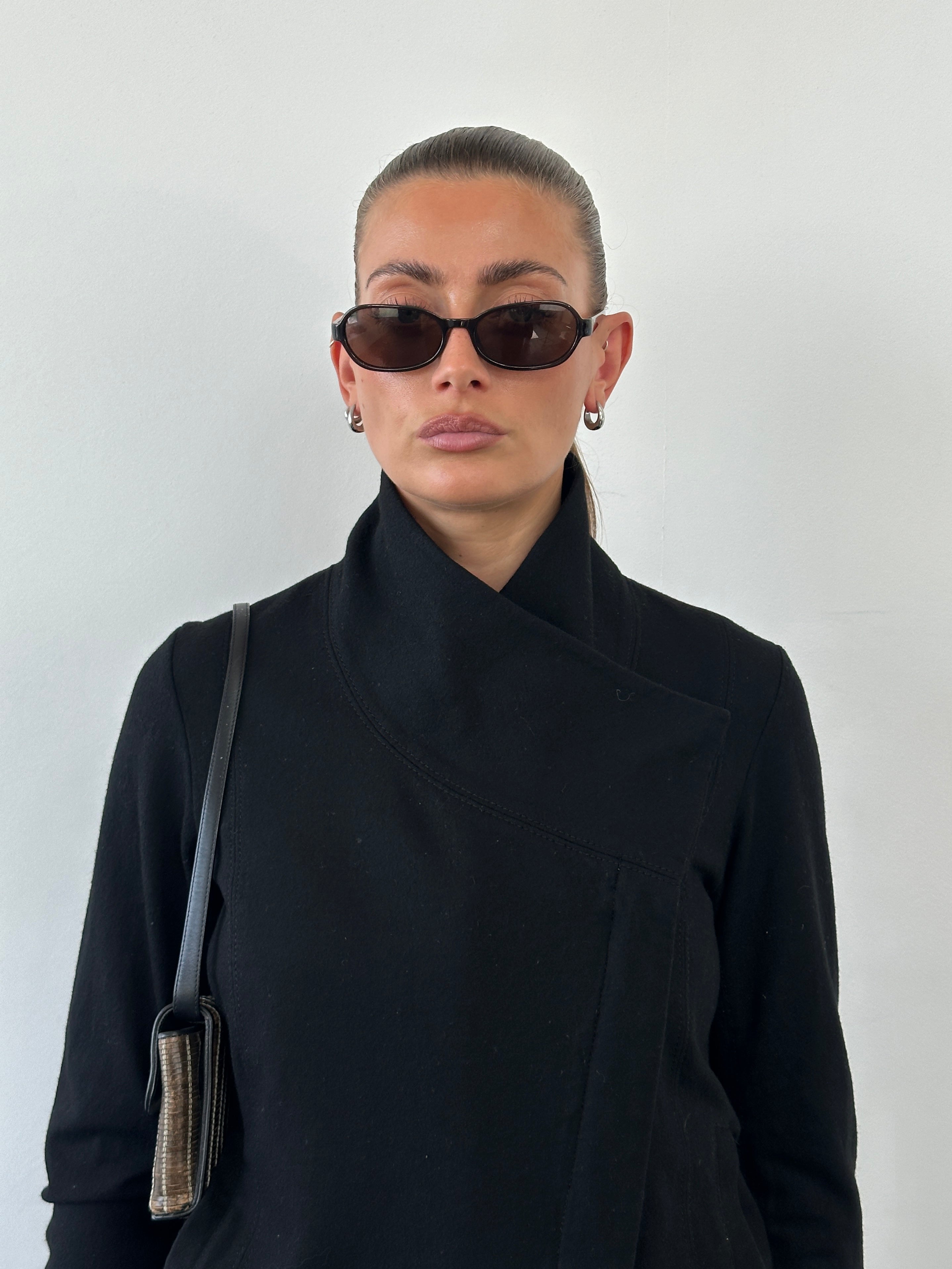 Helmut Lang asymmetric high neck wool belted jacket in black, displayed on a hanger with a modern design.