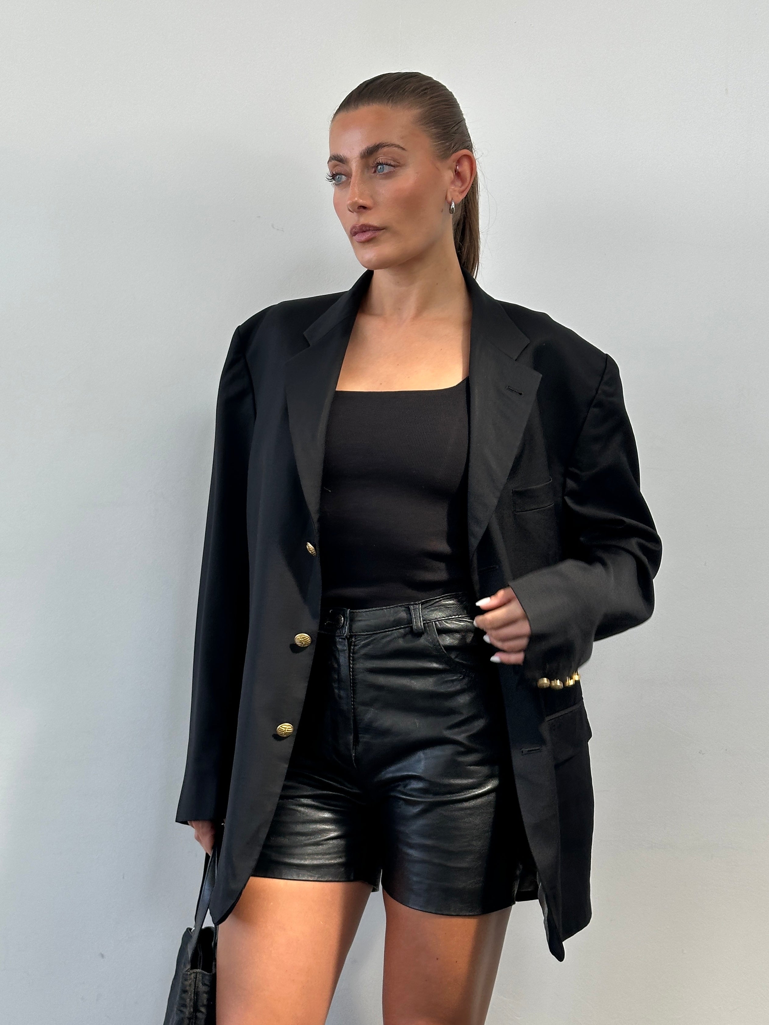 Vintage leather high-waisted mini shorts in W27, showing a close-up of the classic brown leather fabric and high-rise design.
