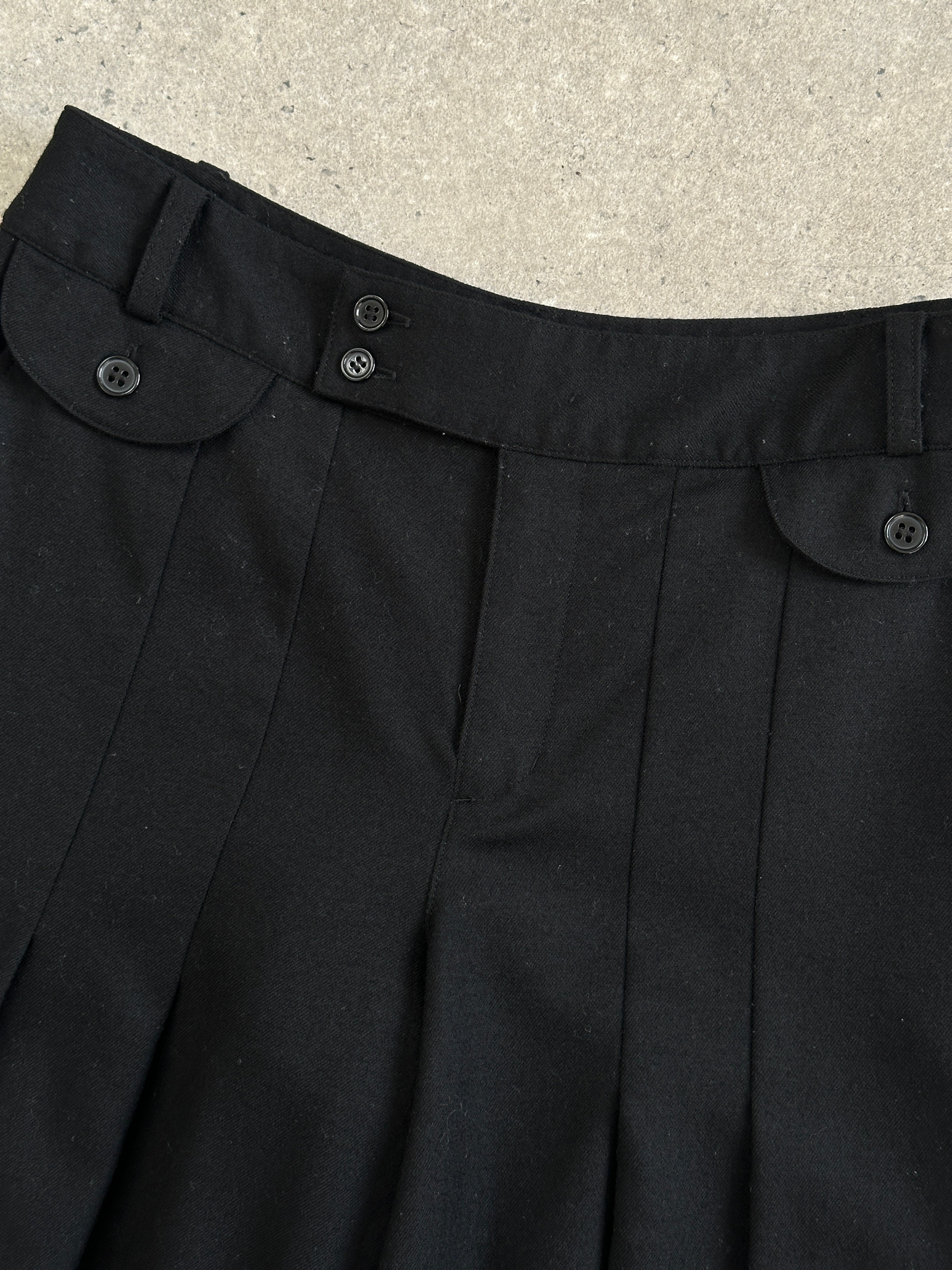 Vintage 1990s wool pleated culottes shorts with high waist and wide leg, displayed on a hanger against a neutral background.