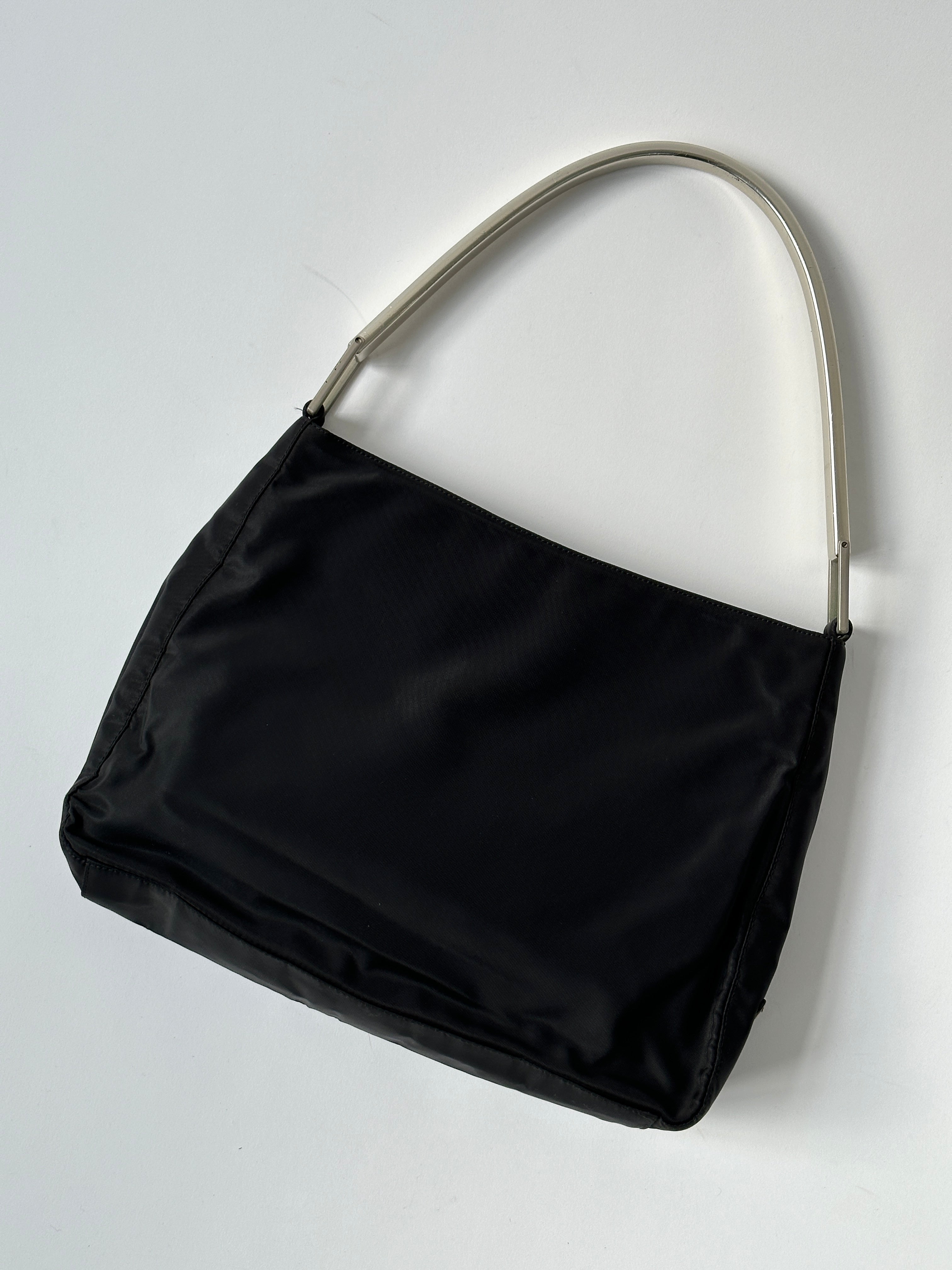 Prada nylon shoulder bag with metal handle, featuring sleek design and durable materials for stylish everyday use.