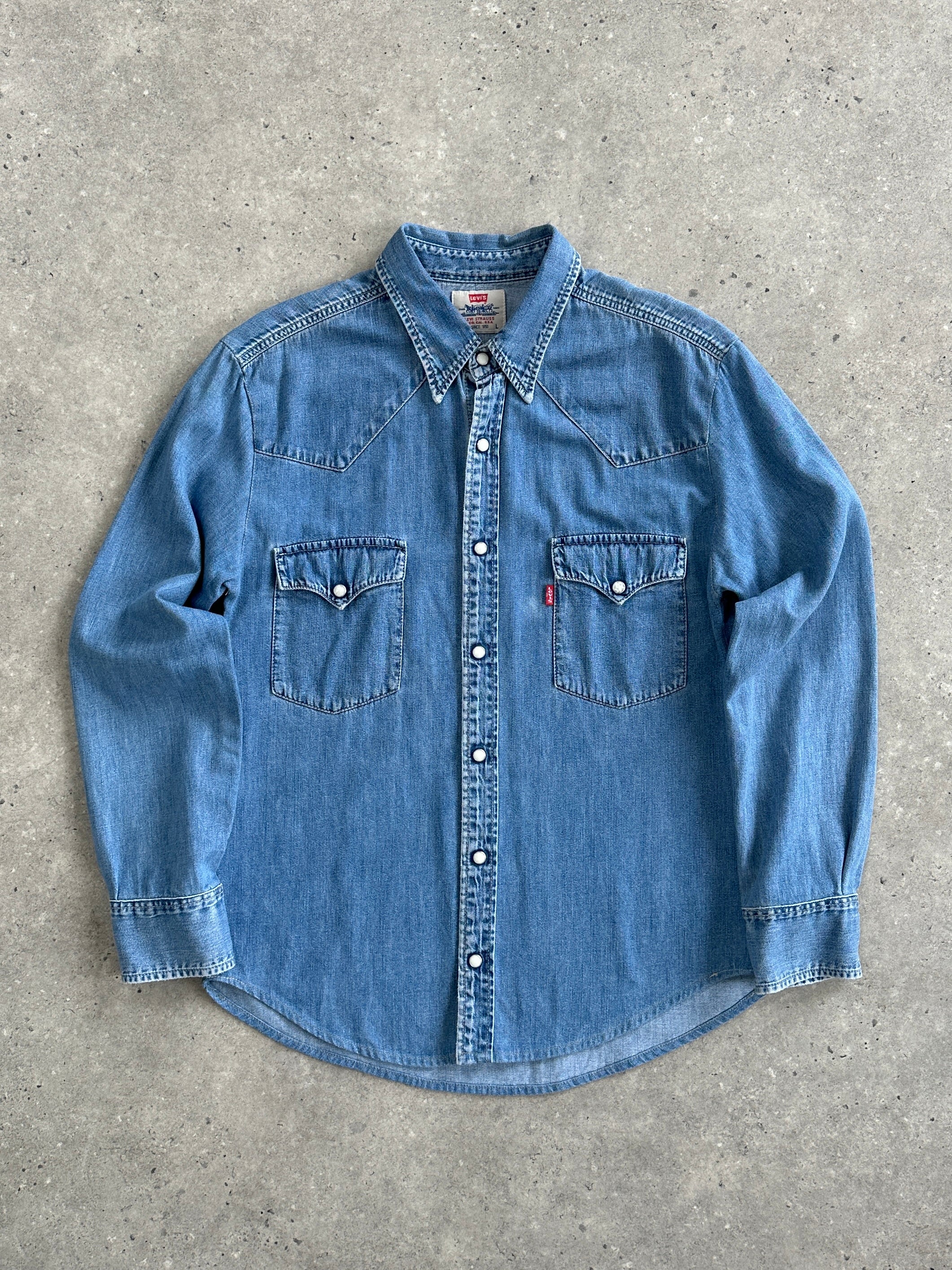 Levi’s cotton button-up denim shirt in size M displayed on a hanger, featuring classic blue denim fabric and button-front design.