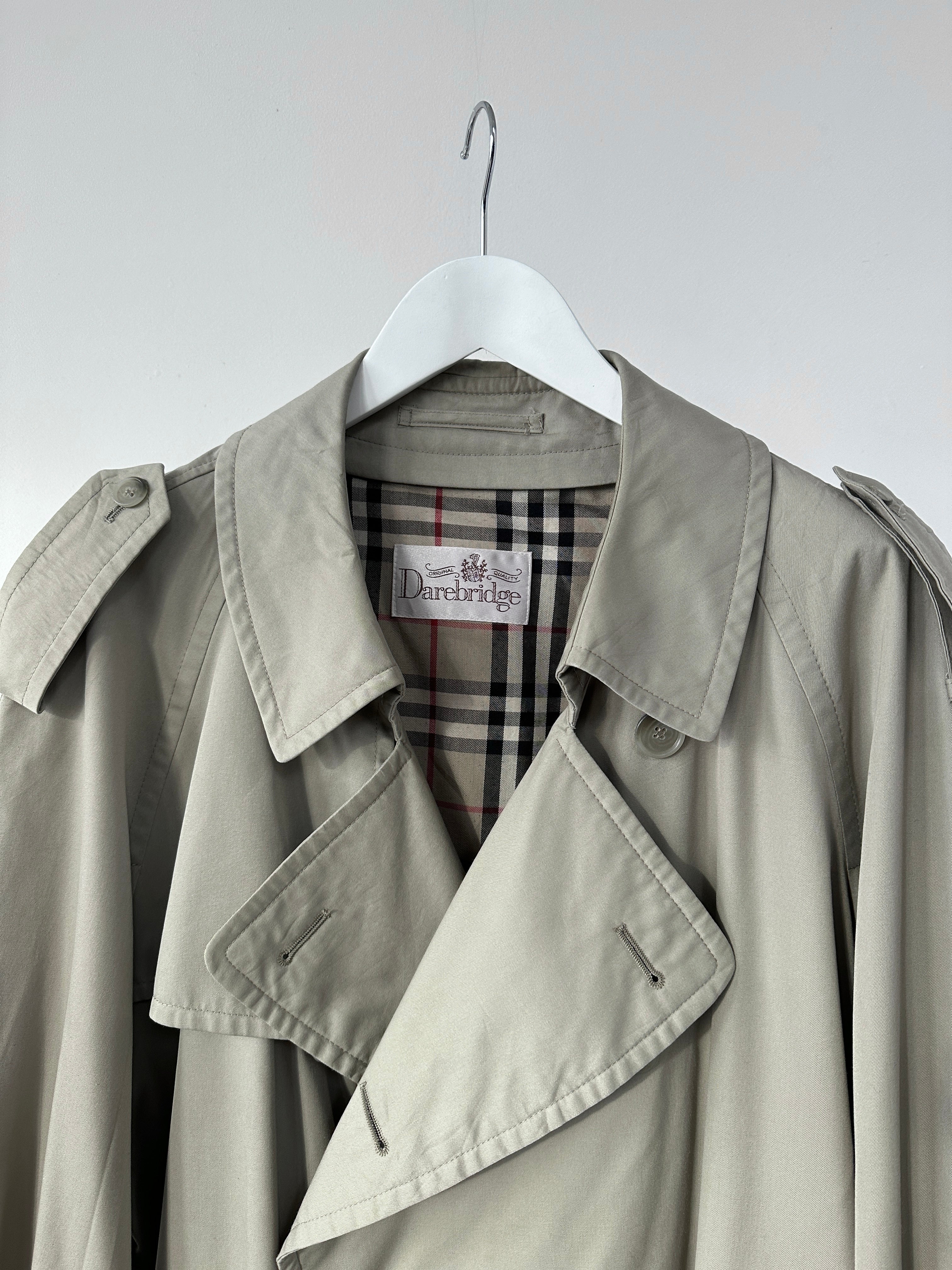 Vintage double-breasted trench coat in XXL size, classic beige color, with wide lapels and belt, displayed on a hanger.