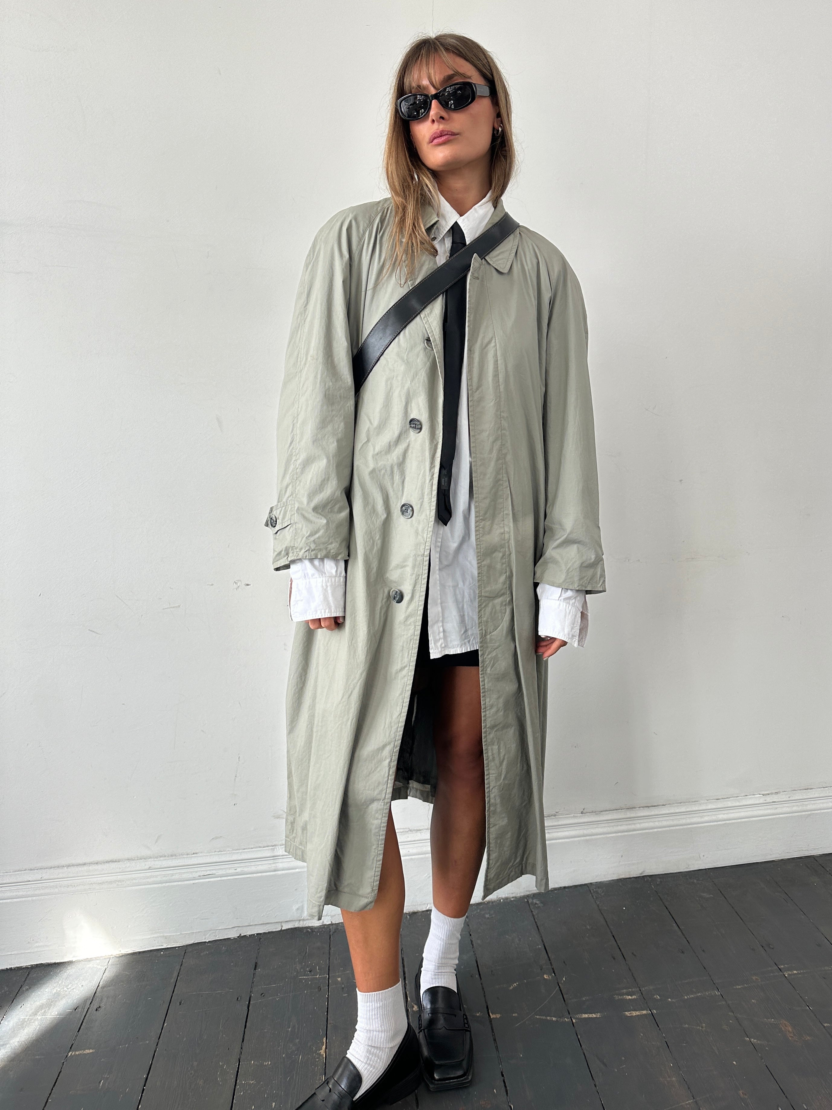 Christian Dior Le Connaisseur belted trench coat in beige, shown on a model with classic collar and double-breasted design.