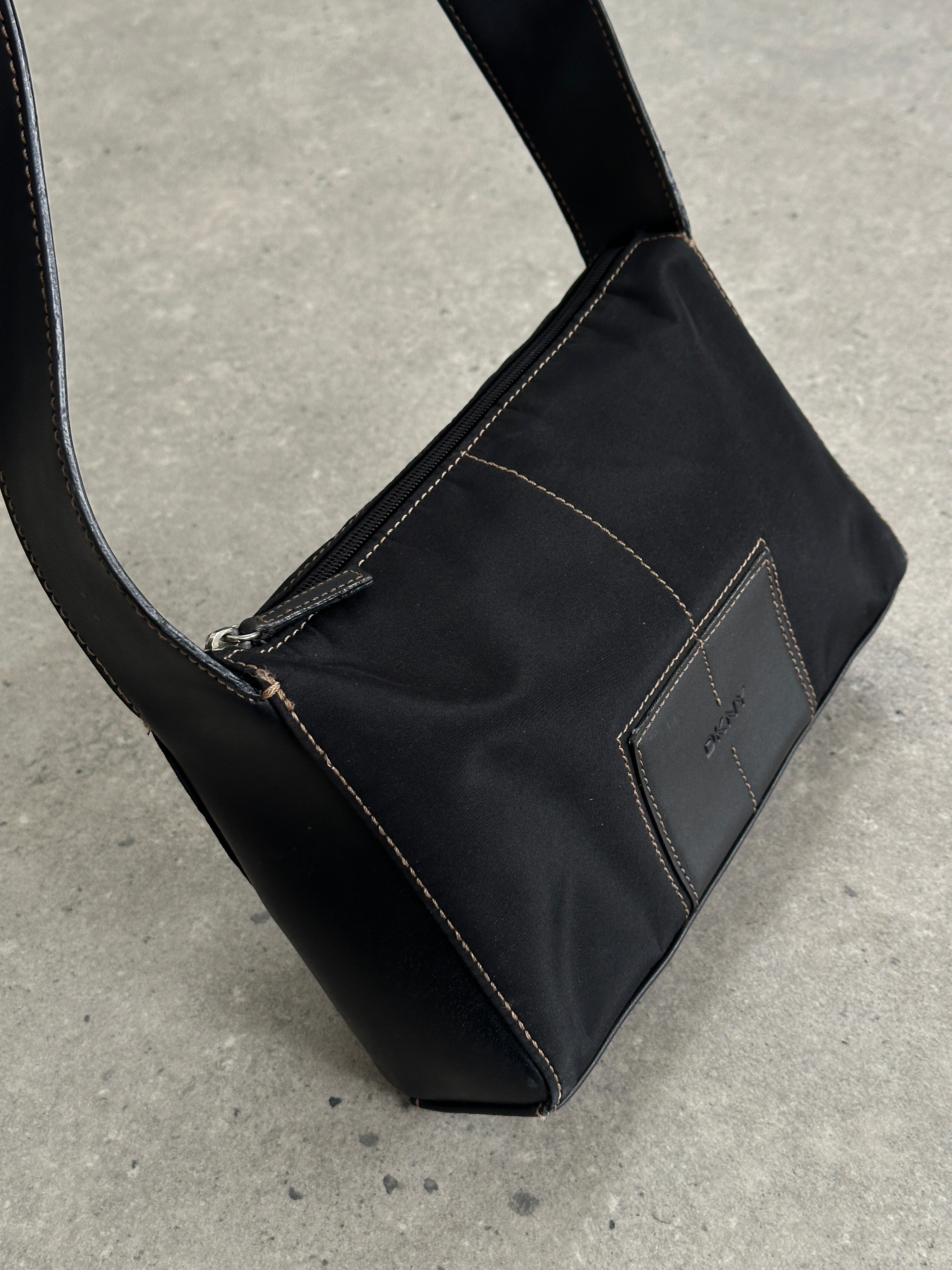 DKNY contrast stitch crossbody bag with adjustable strap and sleek design, featuring stylish stitching and compact size.