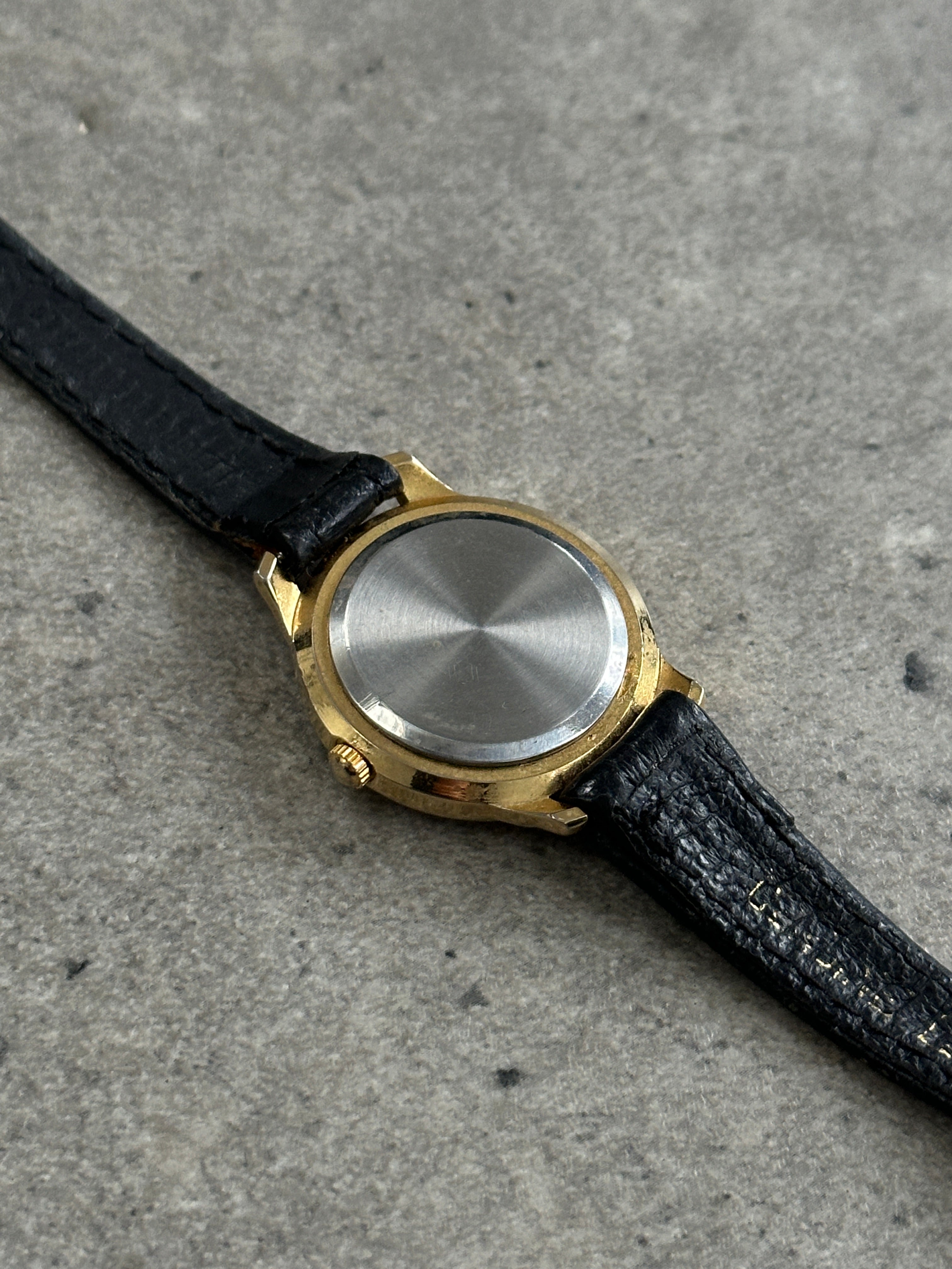 Vintage 1990s gold-tone round quartz watch with a classic design and metal band.