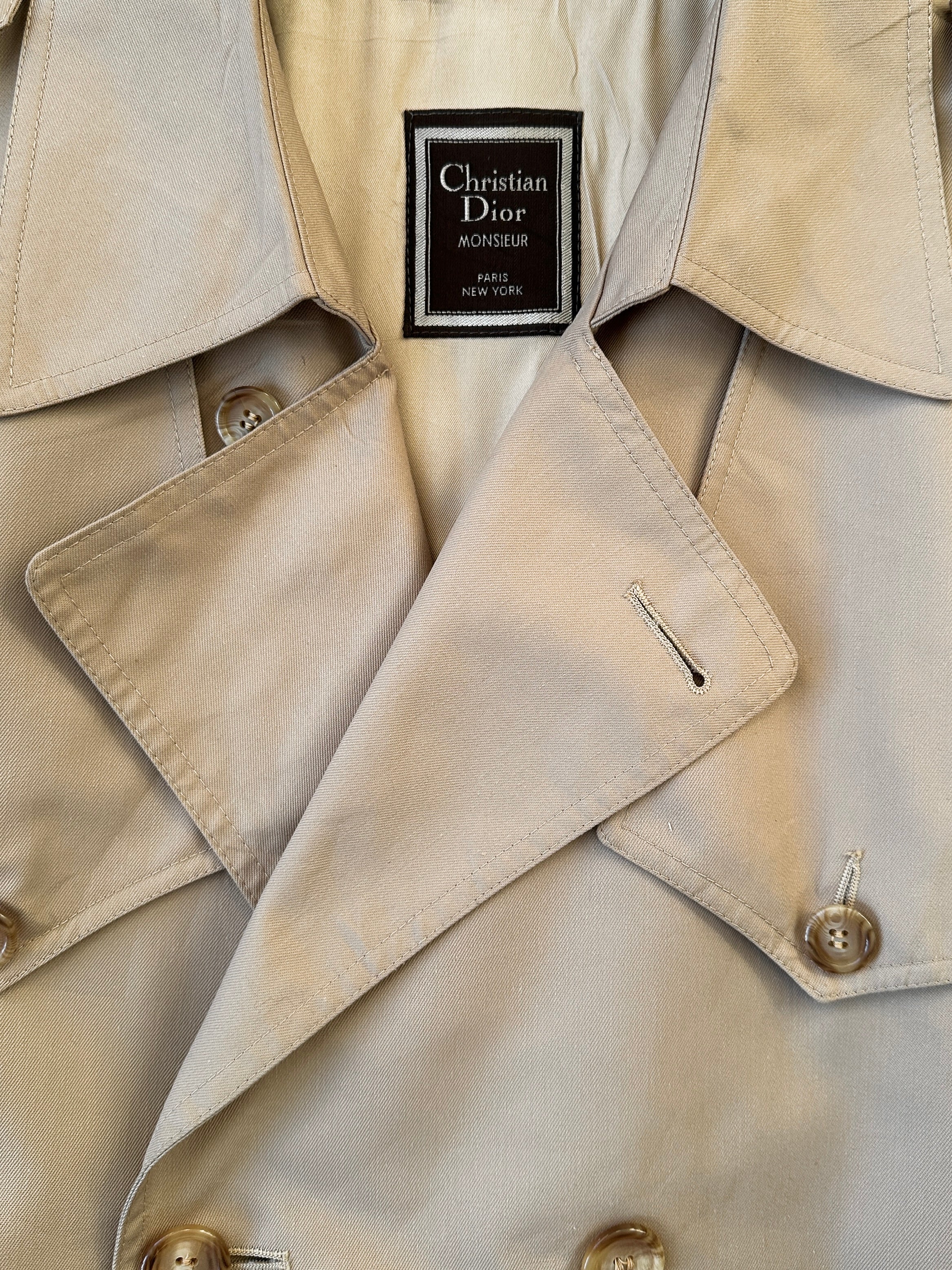 Christian Dior double-breasted cotton trench coat with belted waist, shown in a classic style and neutral color.