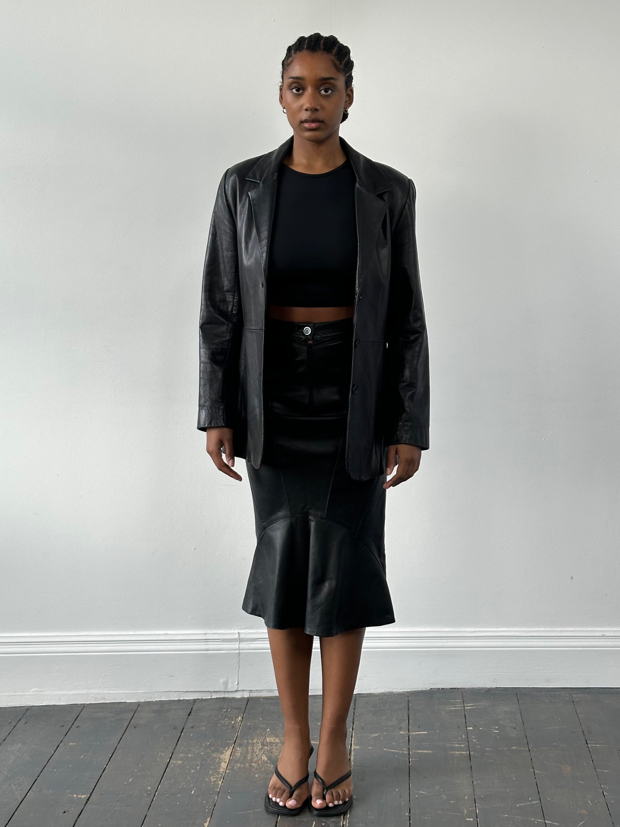 Vintage 1990s leather midi skirt, W25, with classic design and textured brown leather, displayed on a hanger.