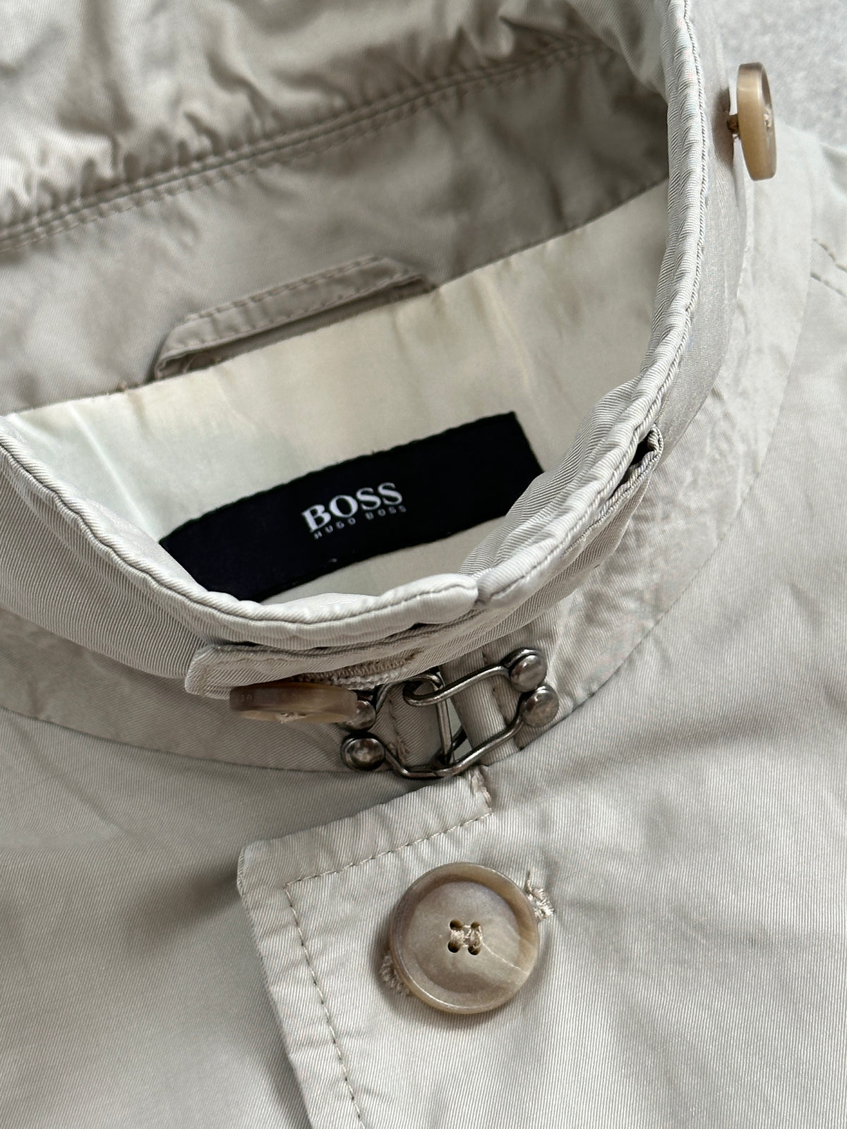 Hugo Boss 2000s high neck belted trench coat in beige, displayed on a hanger with a classic design and belt detail.