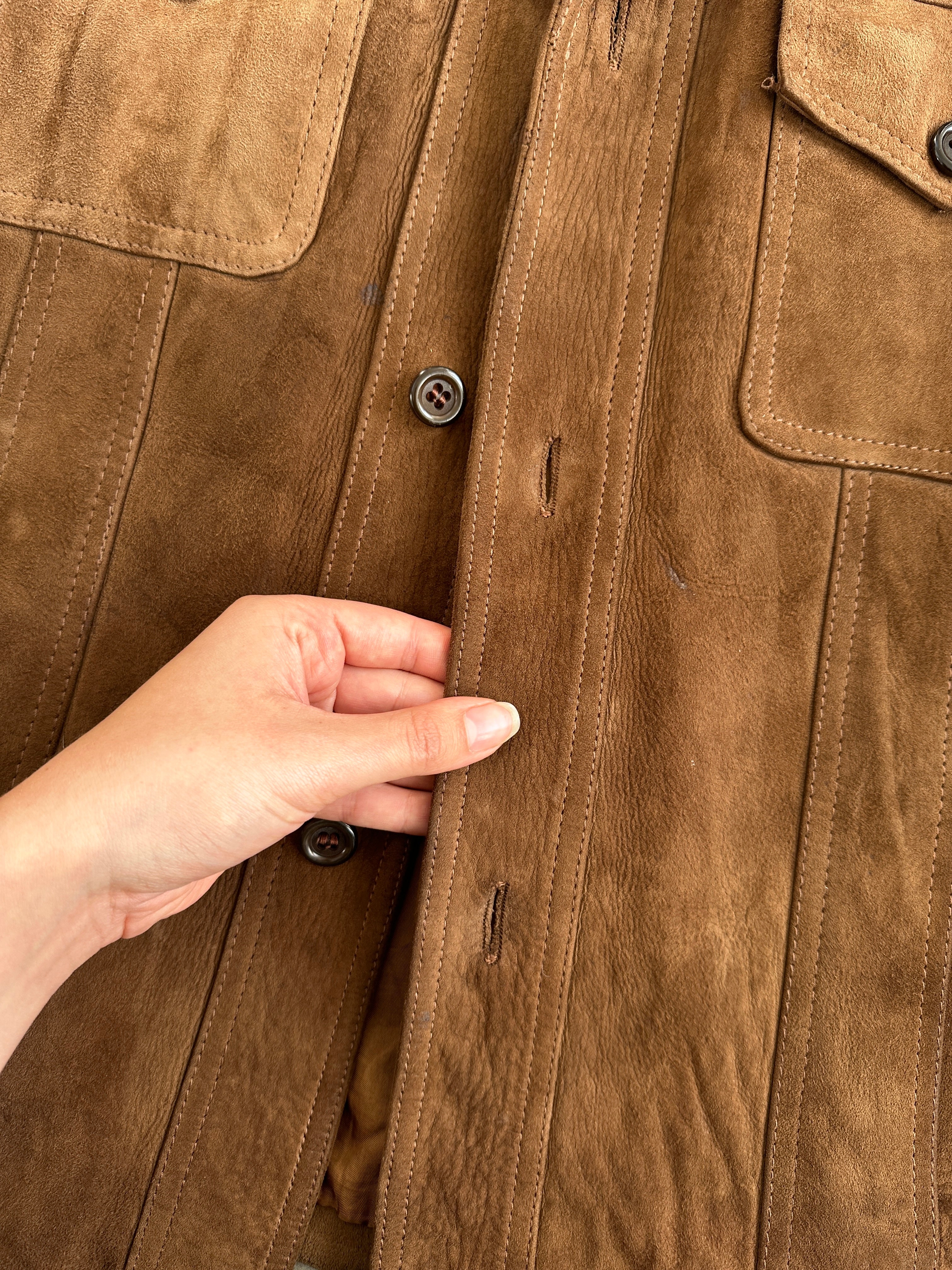 Vintage British 70s suede leather trucker jacket, size large, with classic collar and button details, displayed on a hanger.