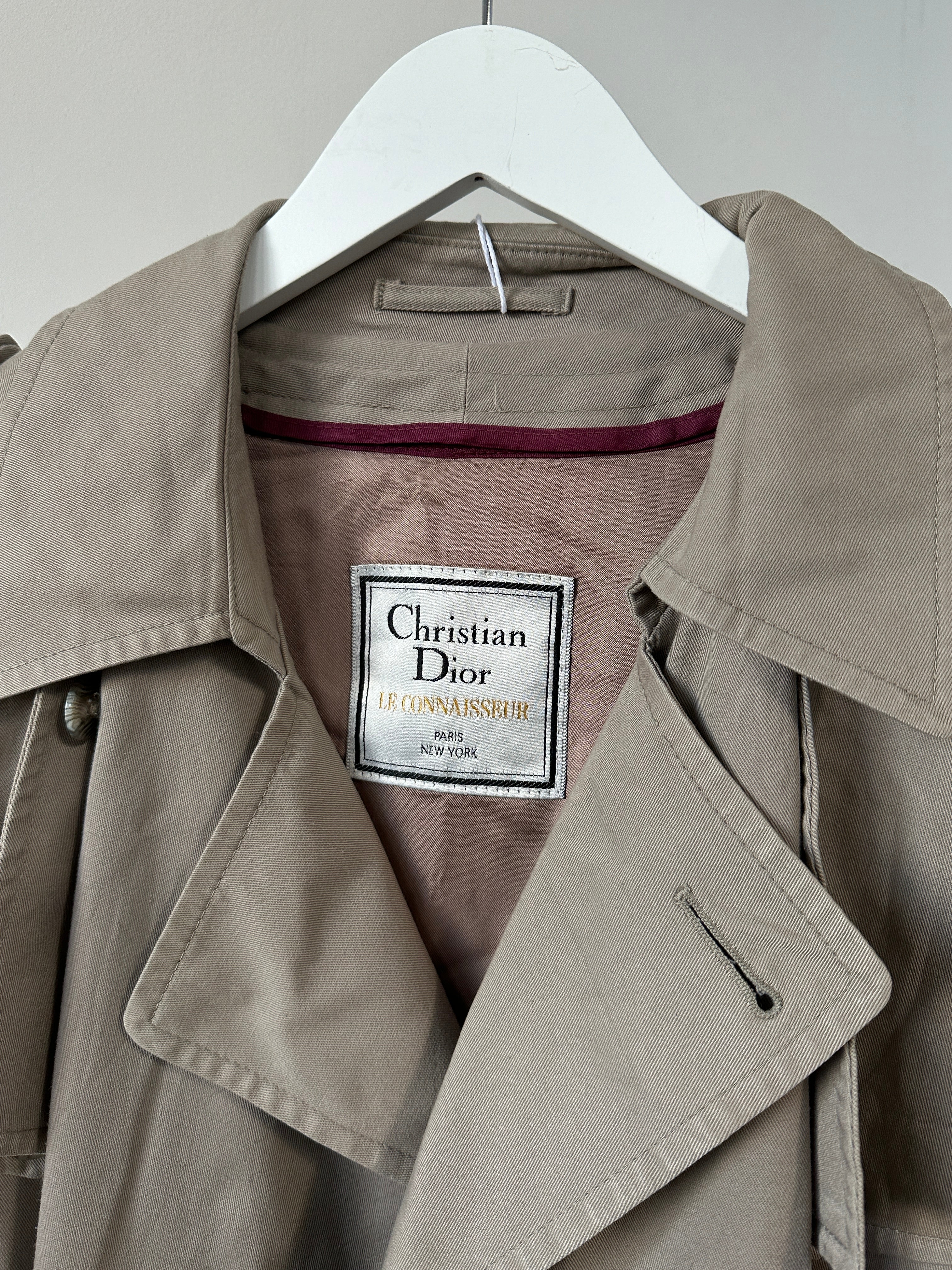 Christian Dior double-breasted cotton trench coat in size L/XL, displayed on a hanger with classic design and neutral color.