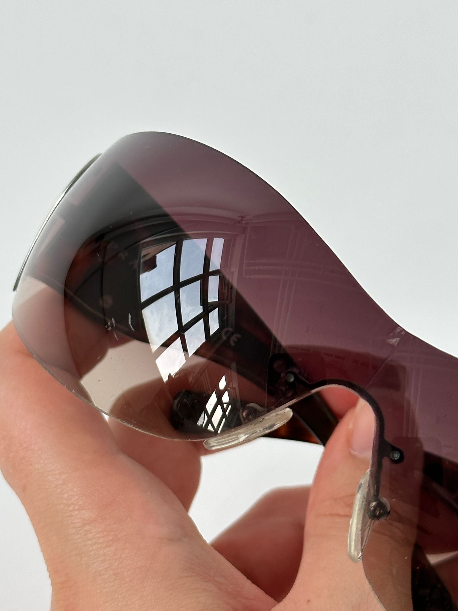 Prada Flame Rimless Wrap Sunglasses with sleek design and dark tinted lenses, showcasing modern eyewear style and brand logo.