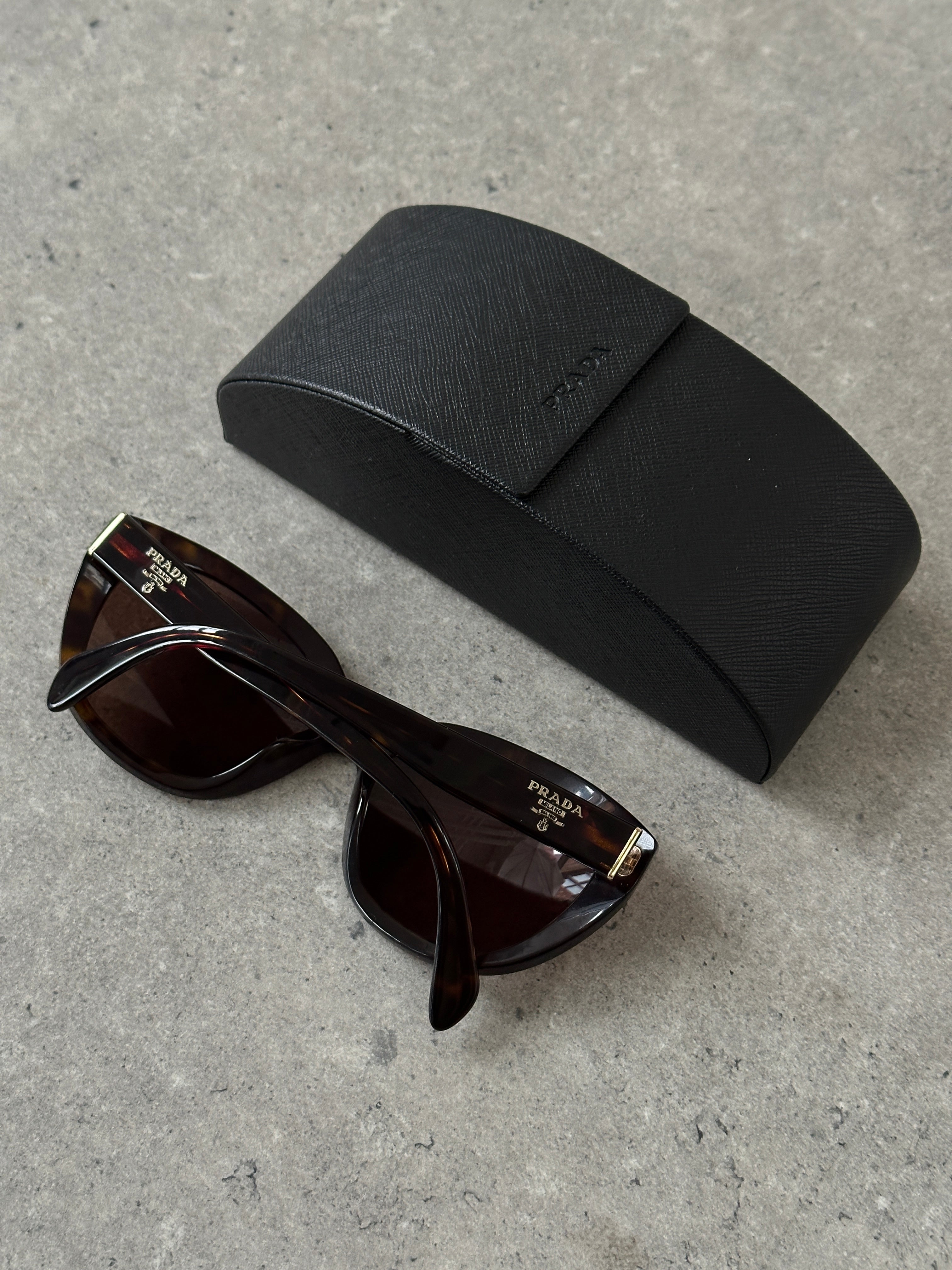 Prada tortoise shell round logo sunglasses with dark lenses and classic frame design.