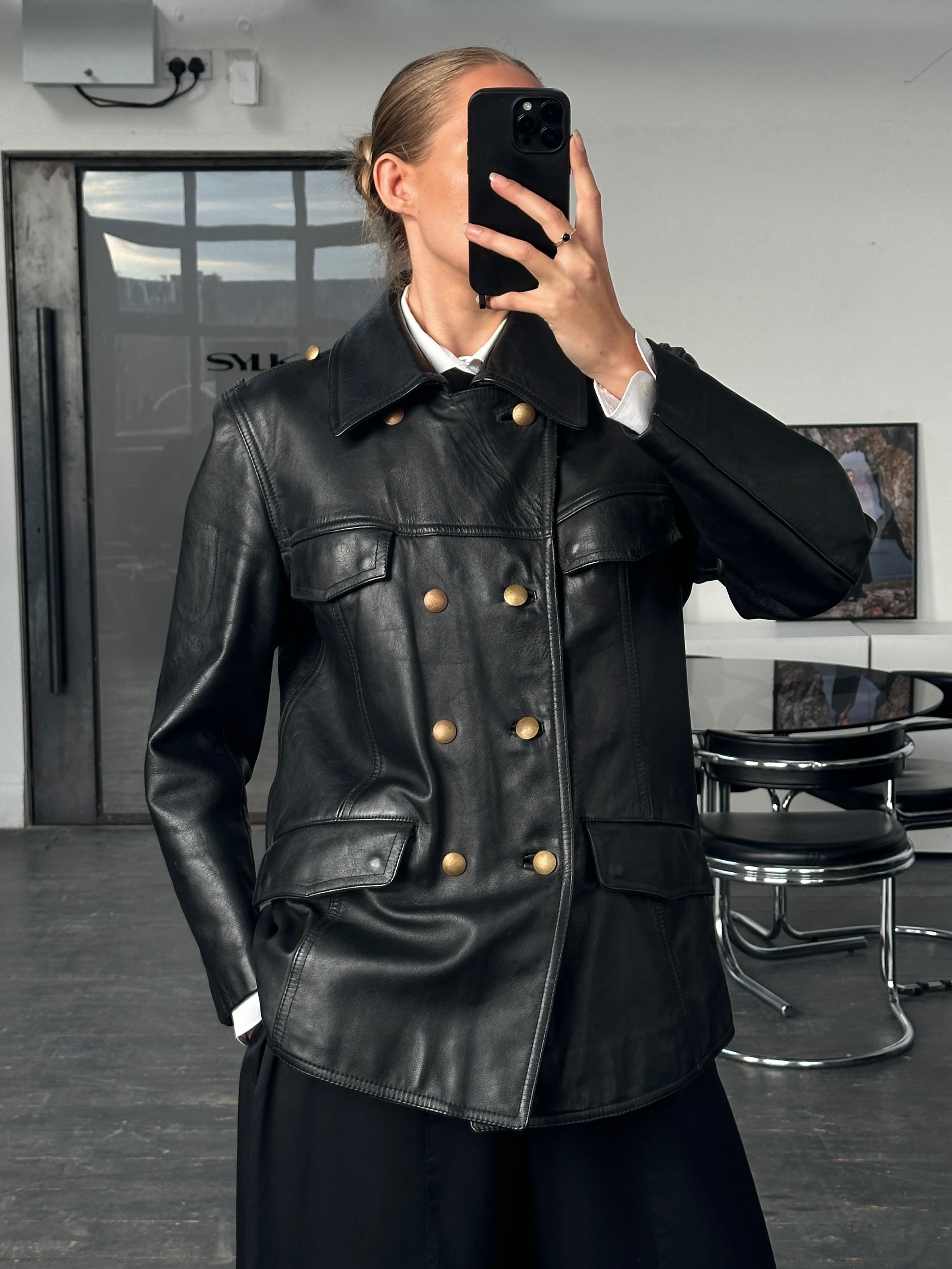 Vintage 1980s double-breasted military leather jacket with epaulets and front pockets, displayed on a hanger.