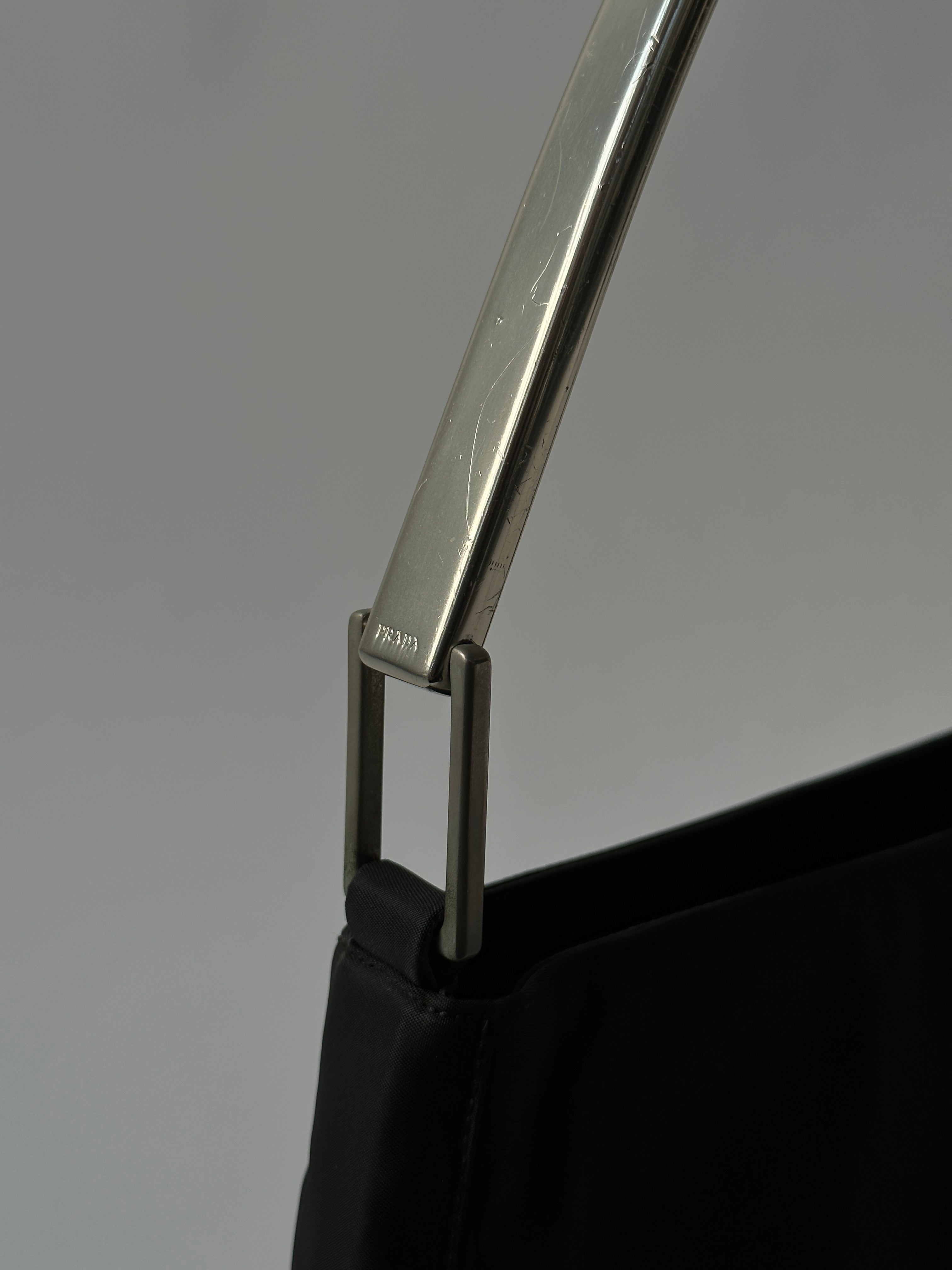 Prada nylon shoulder bag with metal handle and sleek design, featuring a durable strap and minimalist style.