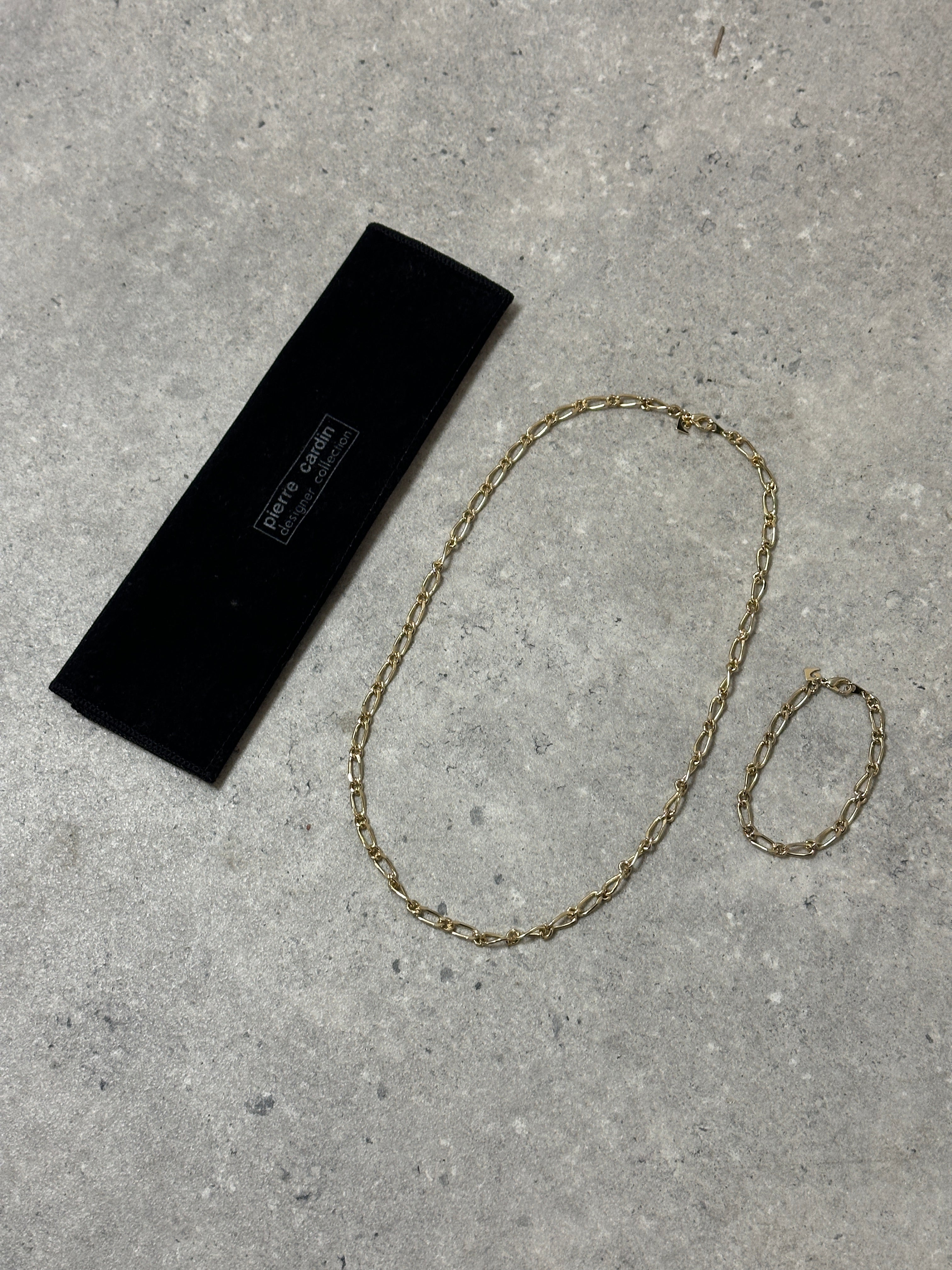 Pierre Cardin gold-plated necklace and bracelet chain set featuring sleek, linked jewelry pieces on a neutral background.