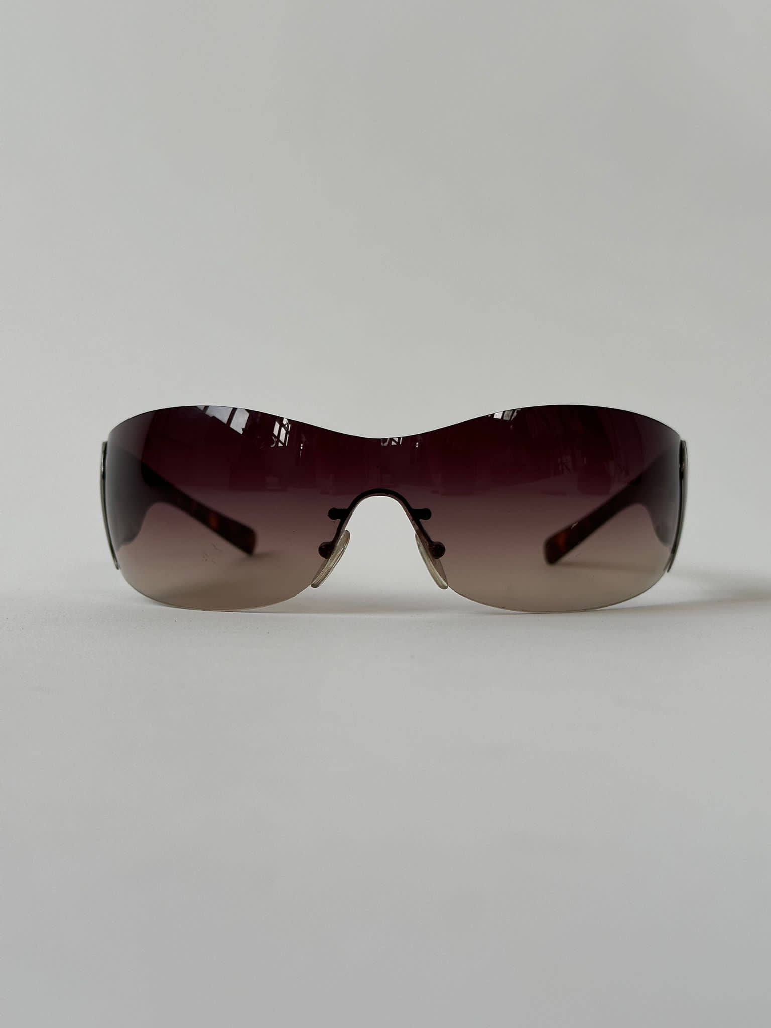 Prada Flame Rimless Wrap Sunglasses with sleek, modern design and tinted lenses, showcasing a stylish and lightweight frame.