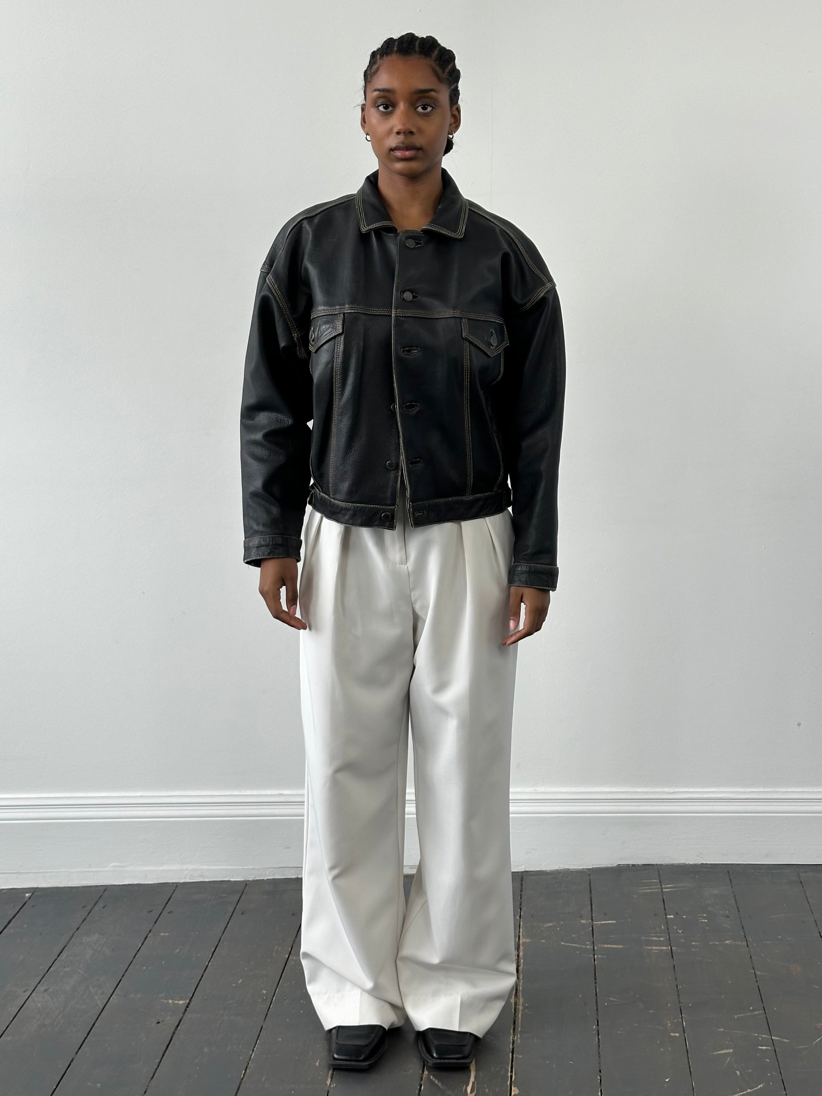 Vintage 1990s leather boxy jacket in black, with structured design and classic style, displayed on a hanger.