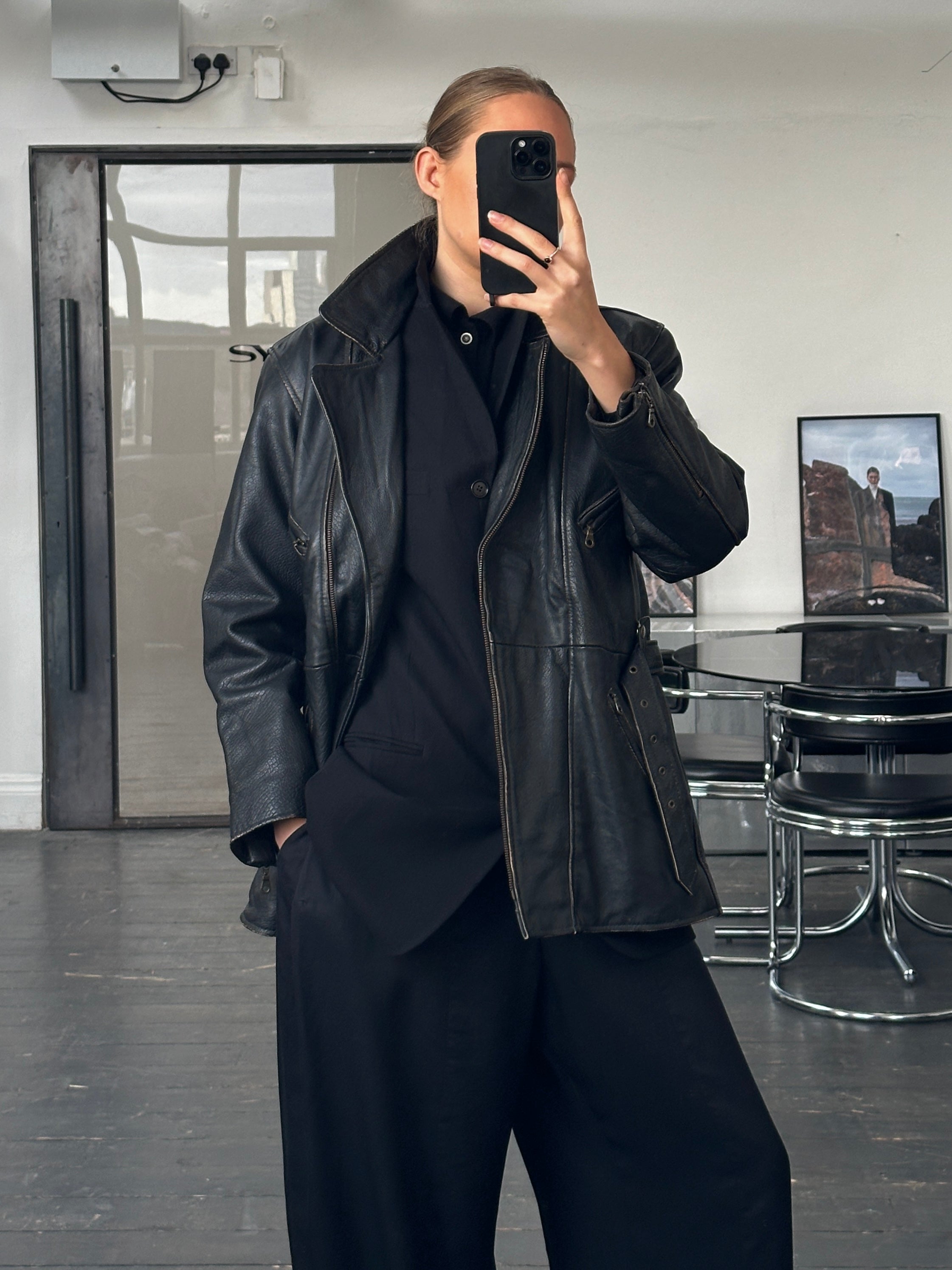 Vintage 1980s aviator belted leather jacket in brown with front zipper and shoulder epaulets, displayed on a hanger.