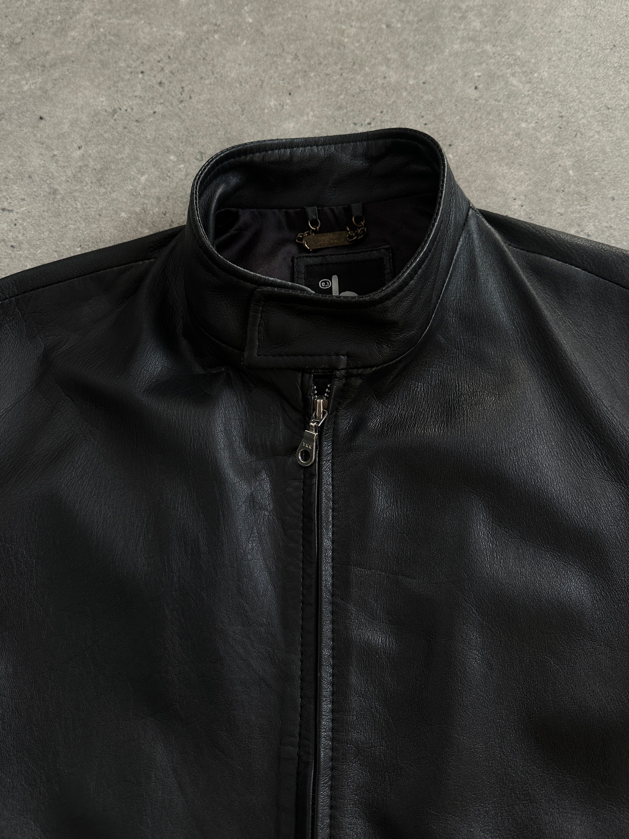 Vintage 2000s minimal high neck leather jacket in black, displayed on a hanger, showcasing its sleek design and classic style.