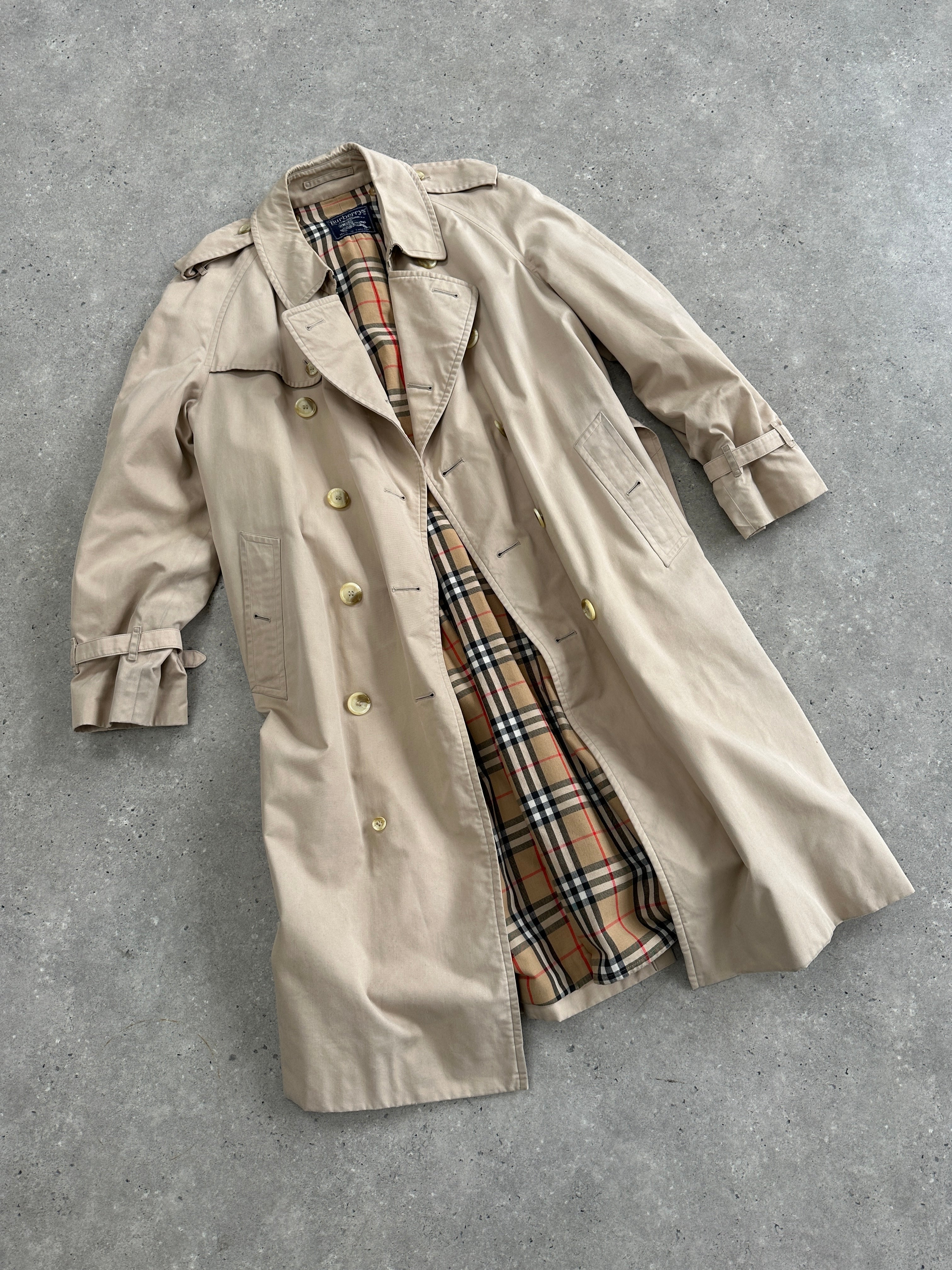Burberry double-breasted trench coat in size XL displayed on a hanger, featuring classic beige color and stylish design.