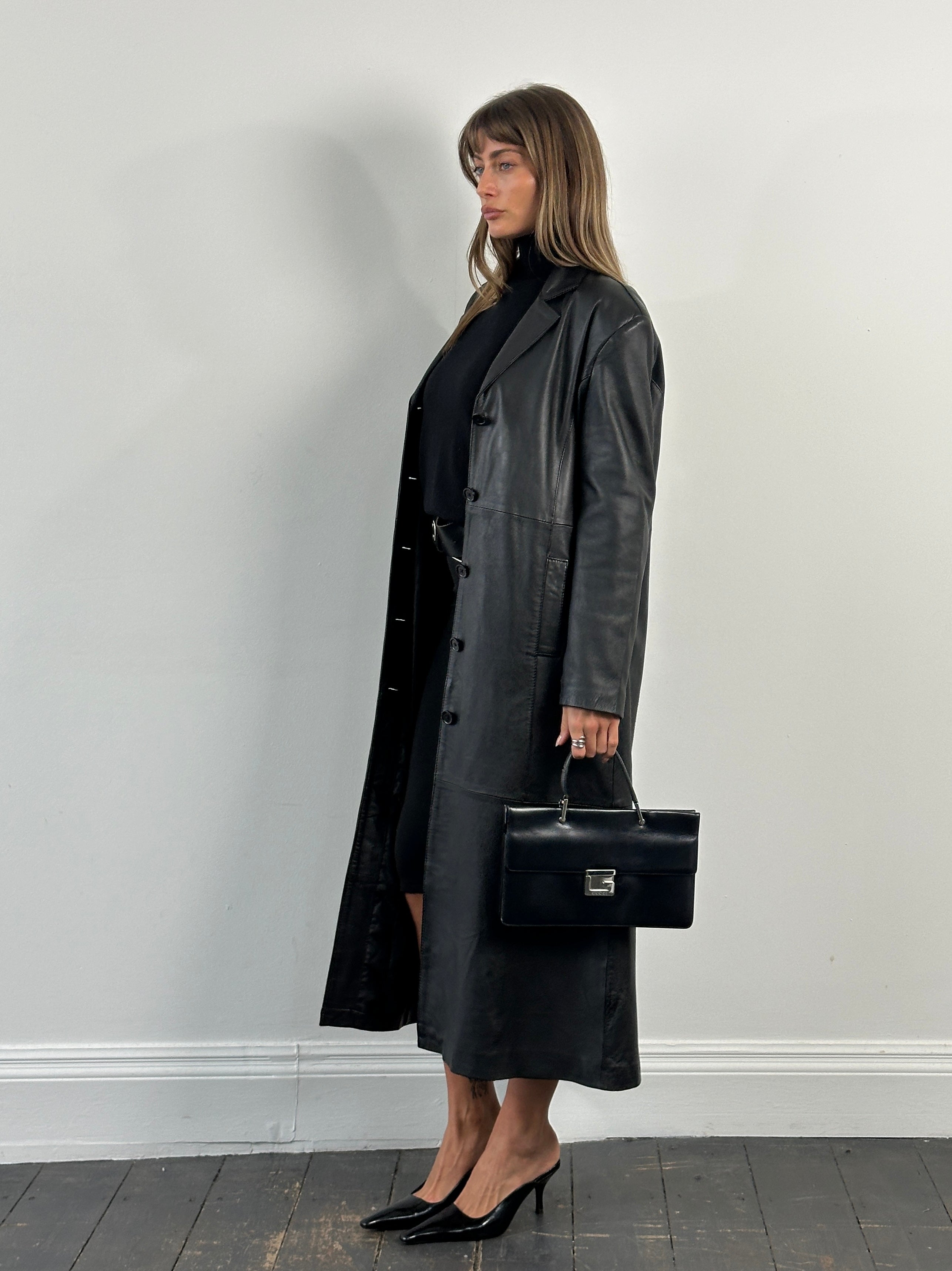 Vintage 1990s floor-length leather trench coat, large size, classic style with belt and wide lapels, shown hanging on a hanger.