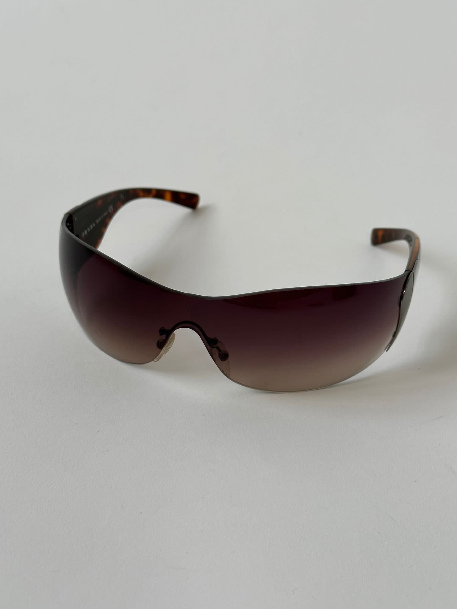 Prada Flame Rimless Wrap Sunglasses with sleek design and clear lenses, featuring a modern, stylish frame.