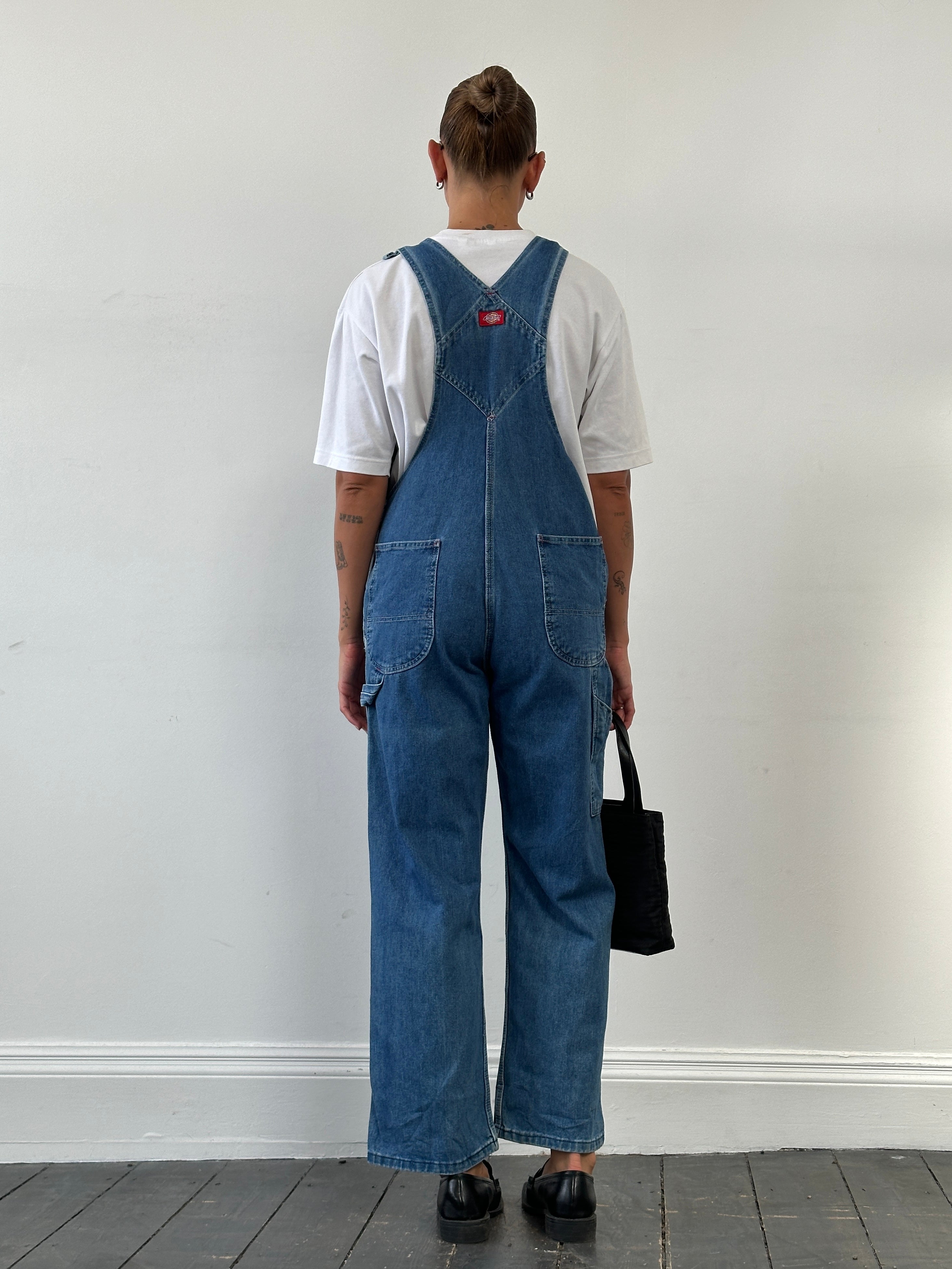 Dickies pure cotton denim dungarees in medium size displayed on a hanger, showing the classic blue denim fabric and adjustable straps.
