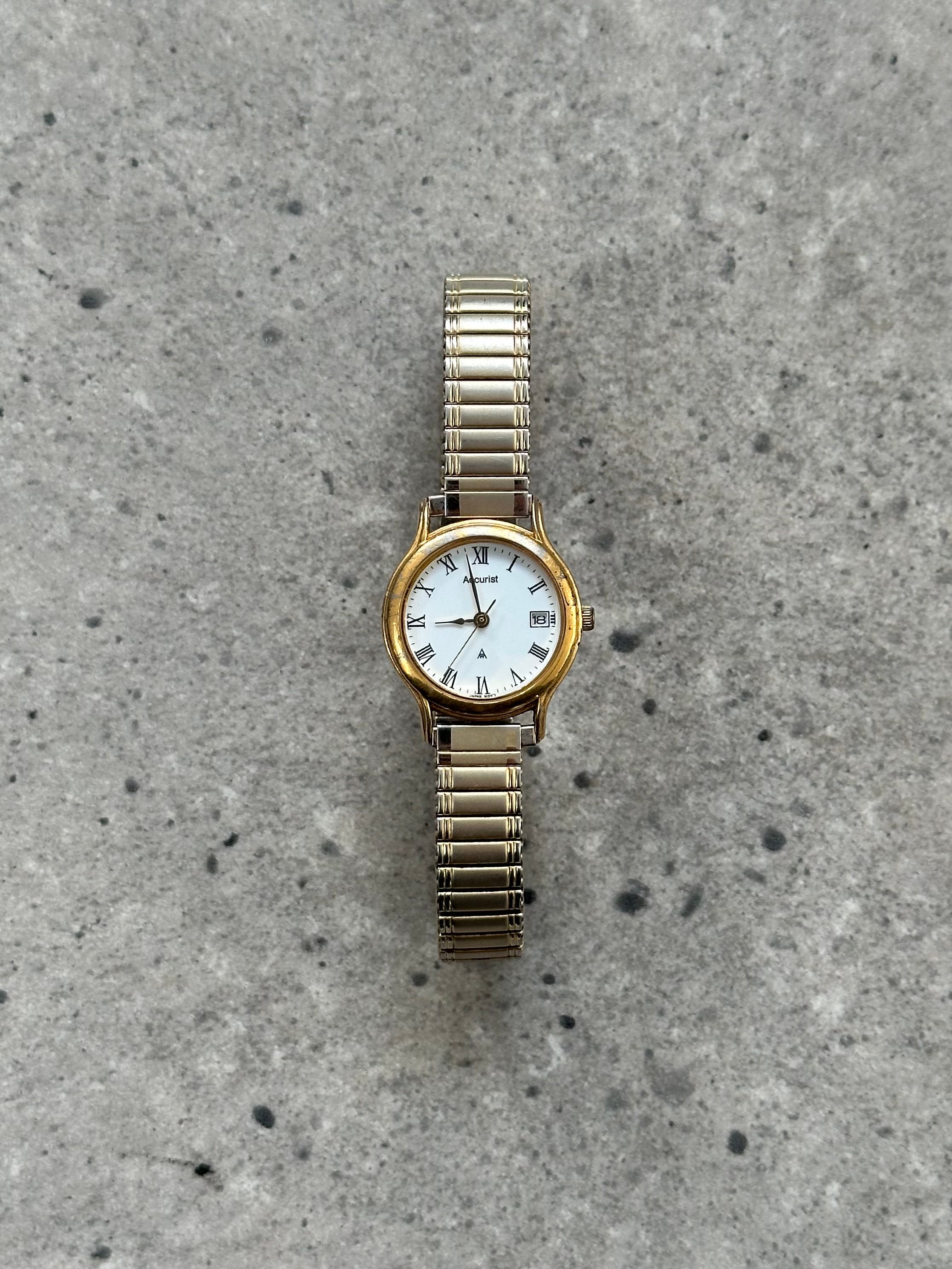 Accurist 1990s gold tone quartz watch with classic round face and metal bracelet, vintage style timepiece.