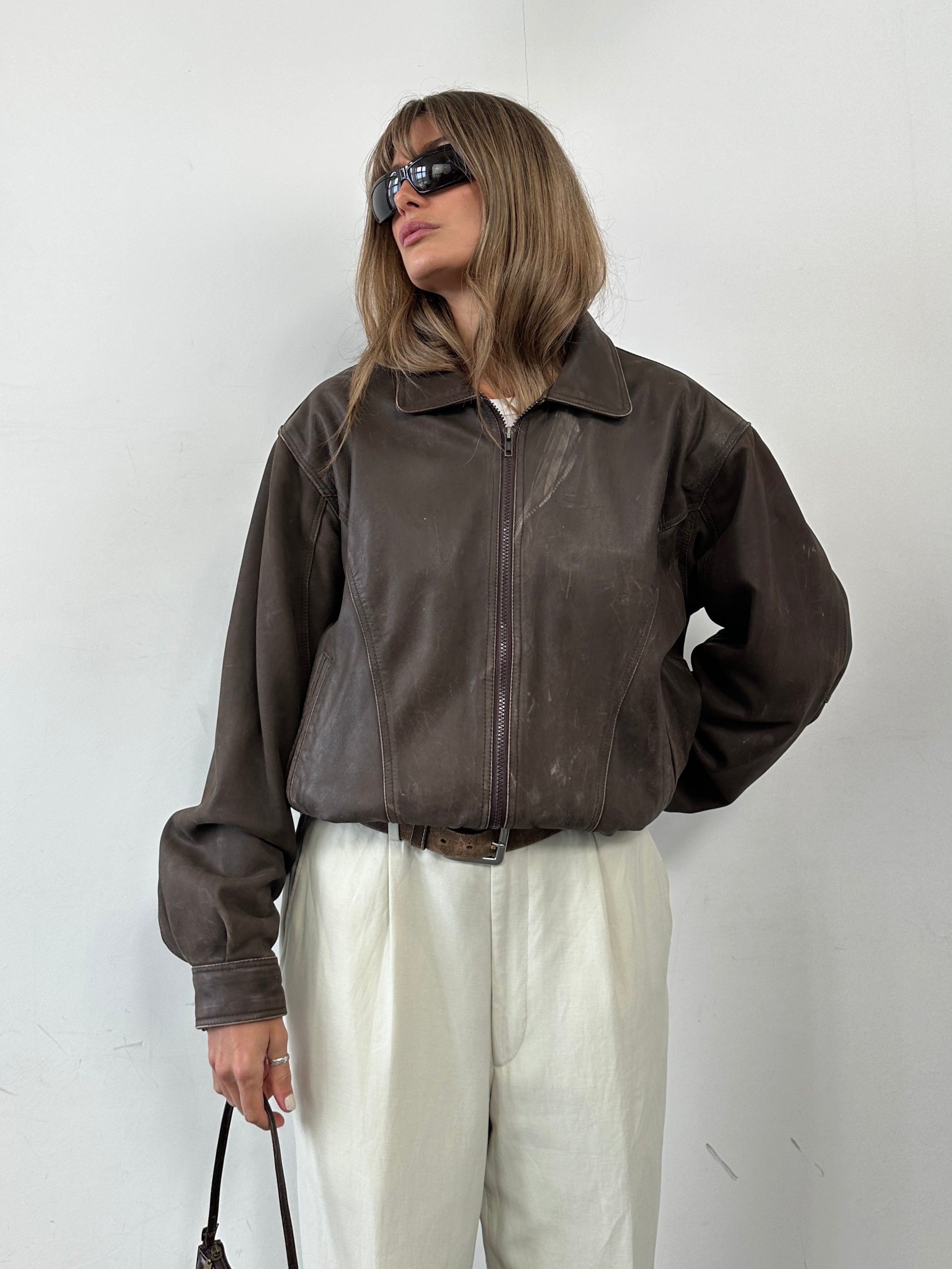 Vintage distressed leather bomber jacket in size M, featuring a rugged design and classic style, displayed on a hanger.