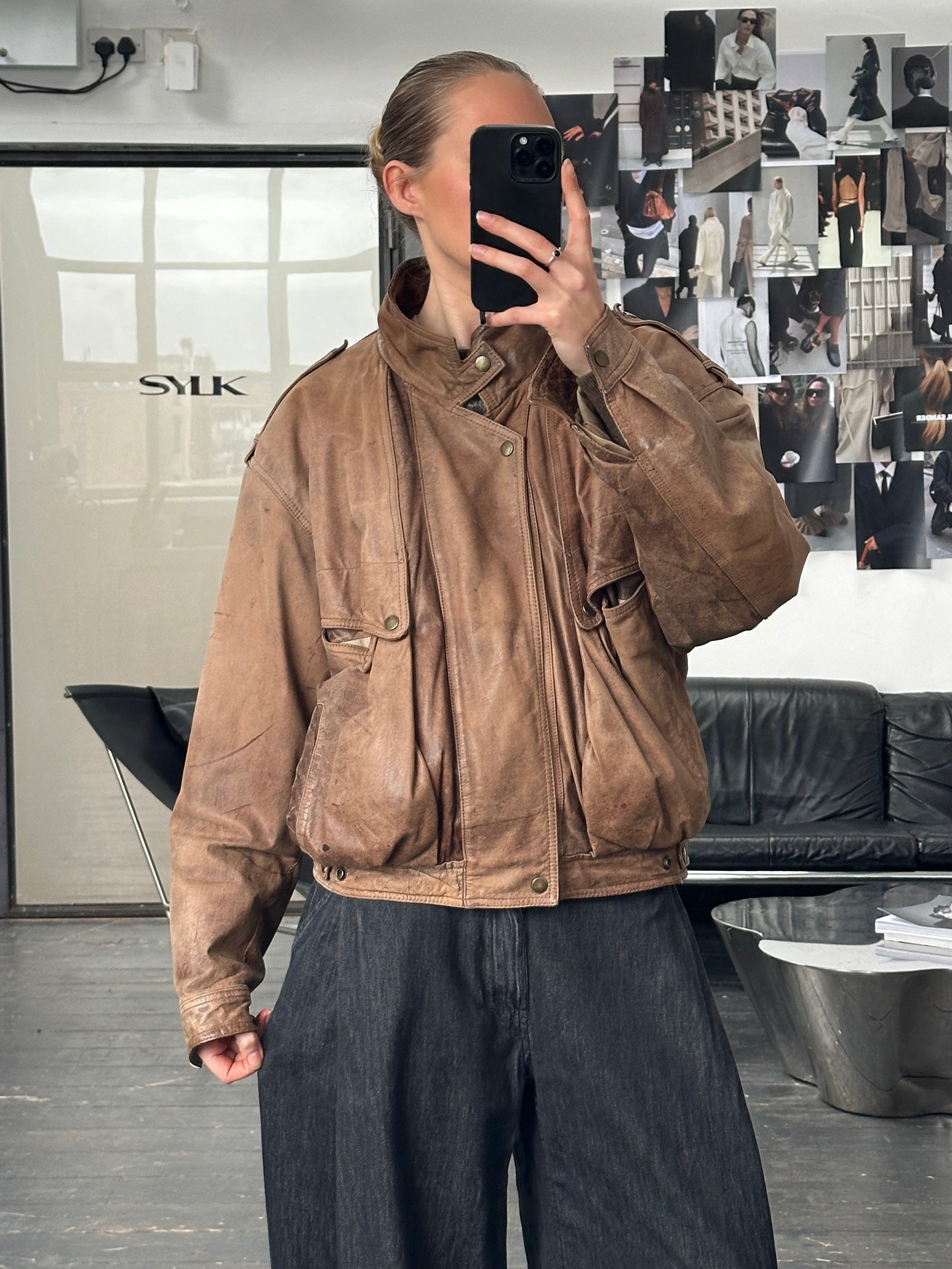 Vintage 1990s high neck aged leather bomber jacket displayed on a hanger, showcasing its vintage style and aged leather texture.