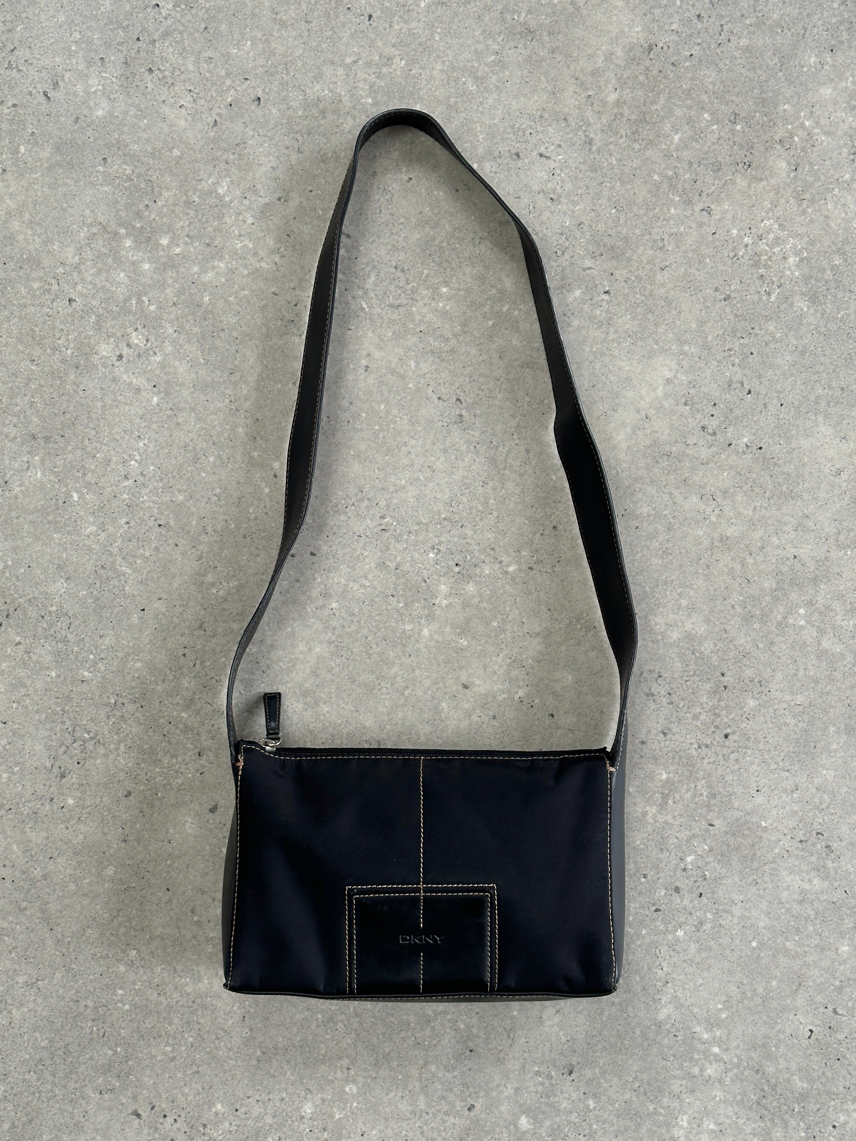 DKNY contrast stitch crossbody bag with adjustable strap and sleek design, featuring stylish stitching details.