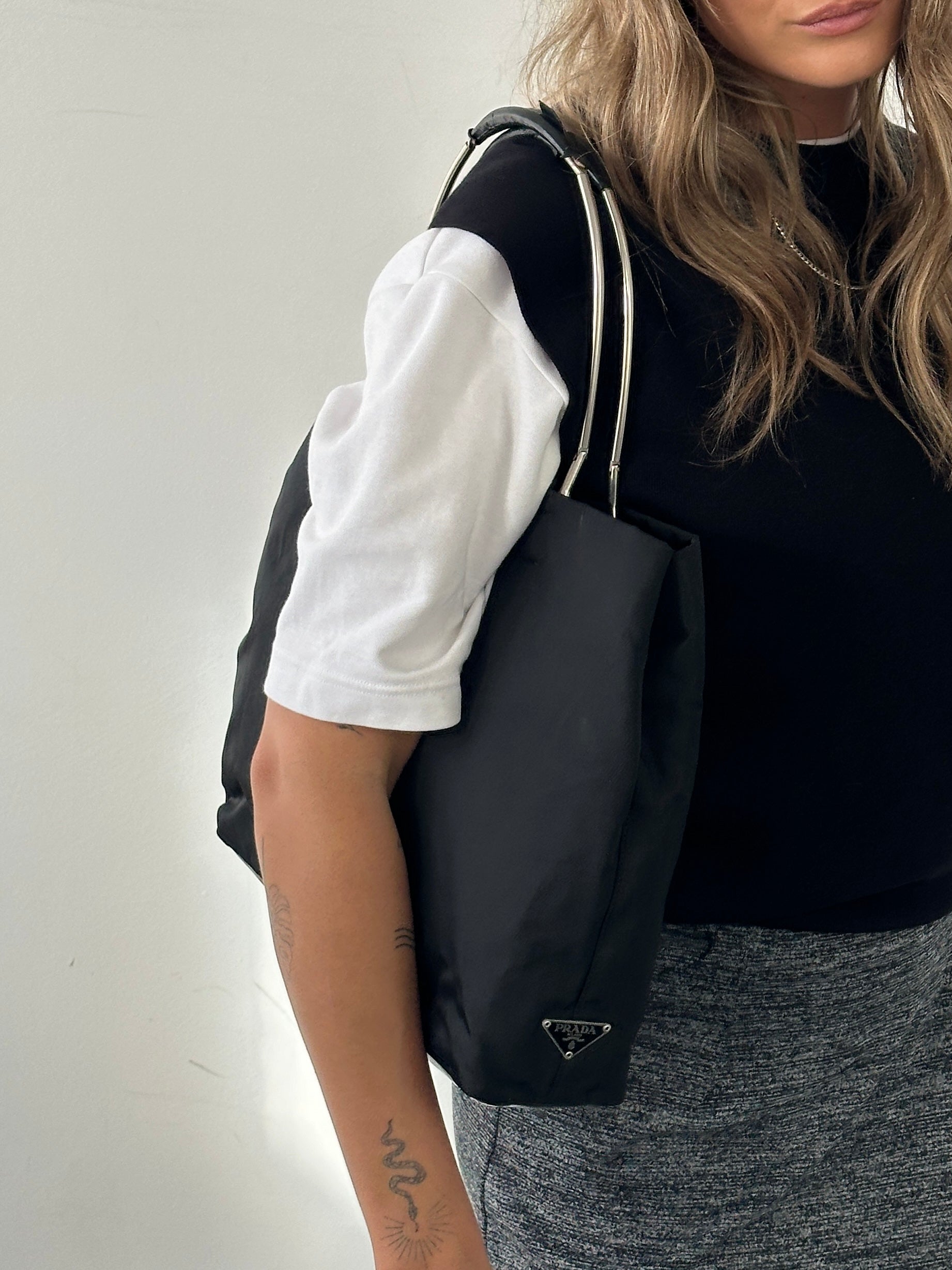 Prada nylon leather tote bag with dual top handles and spacious interior, shown in a sleek black design.