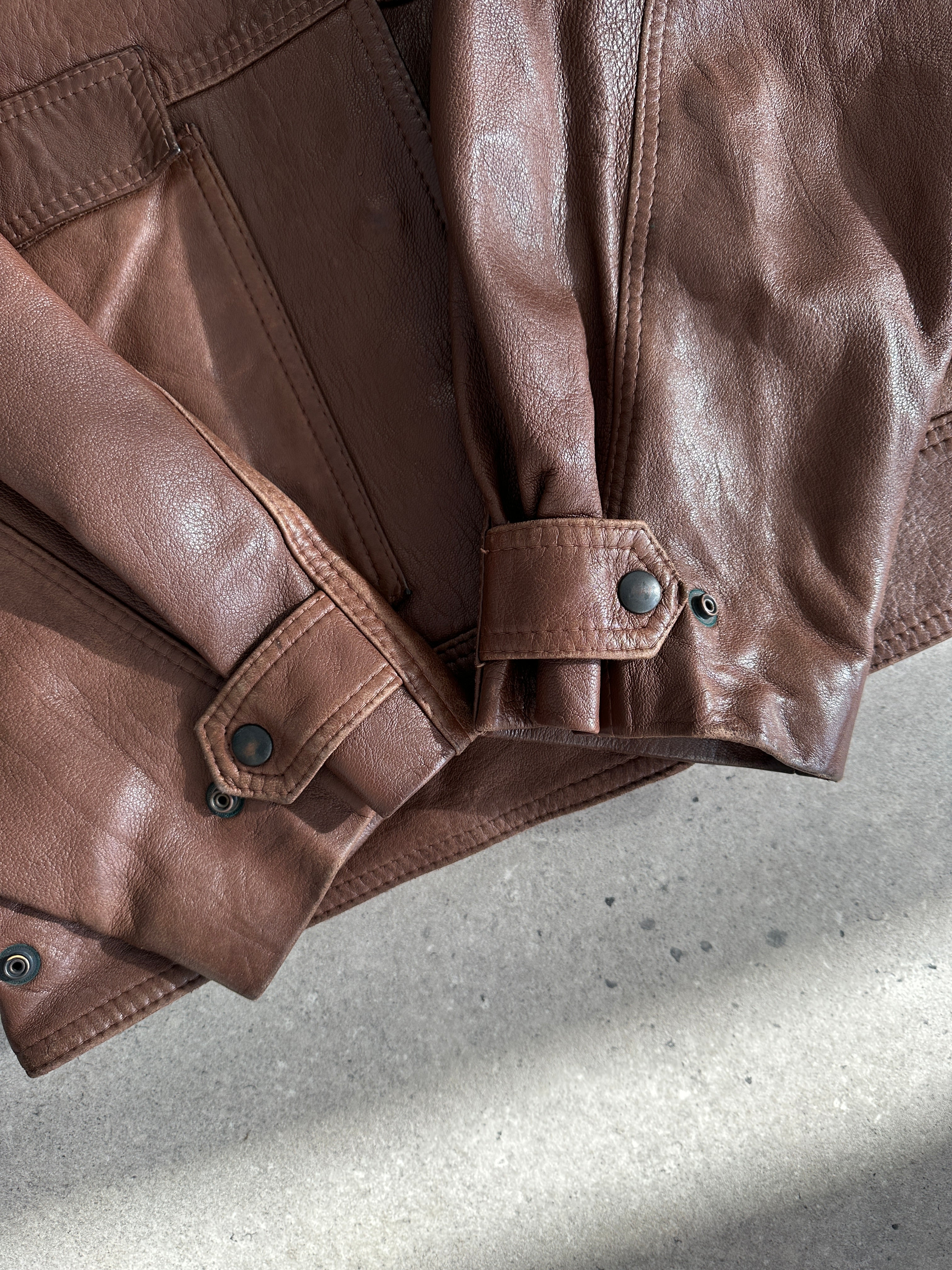 Vintage cropped leather jacket in black, featuring classic design and silver hardware, displayed on a hanger.