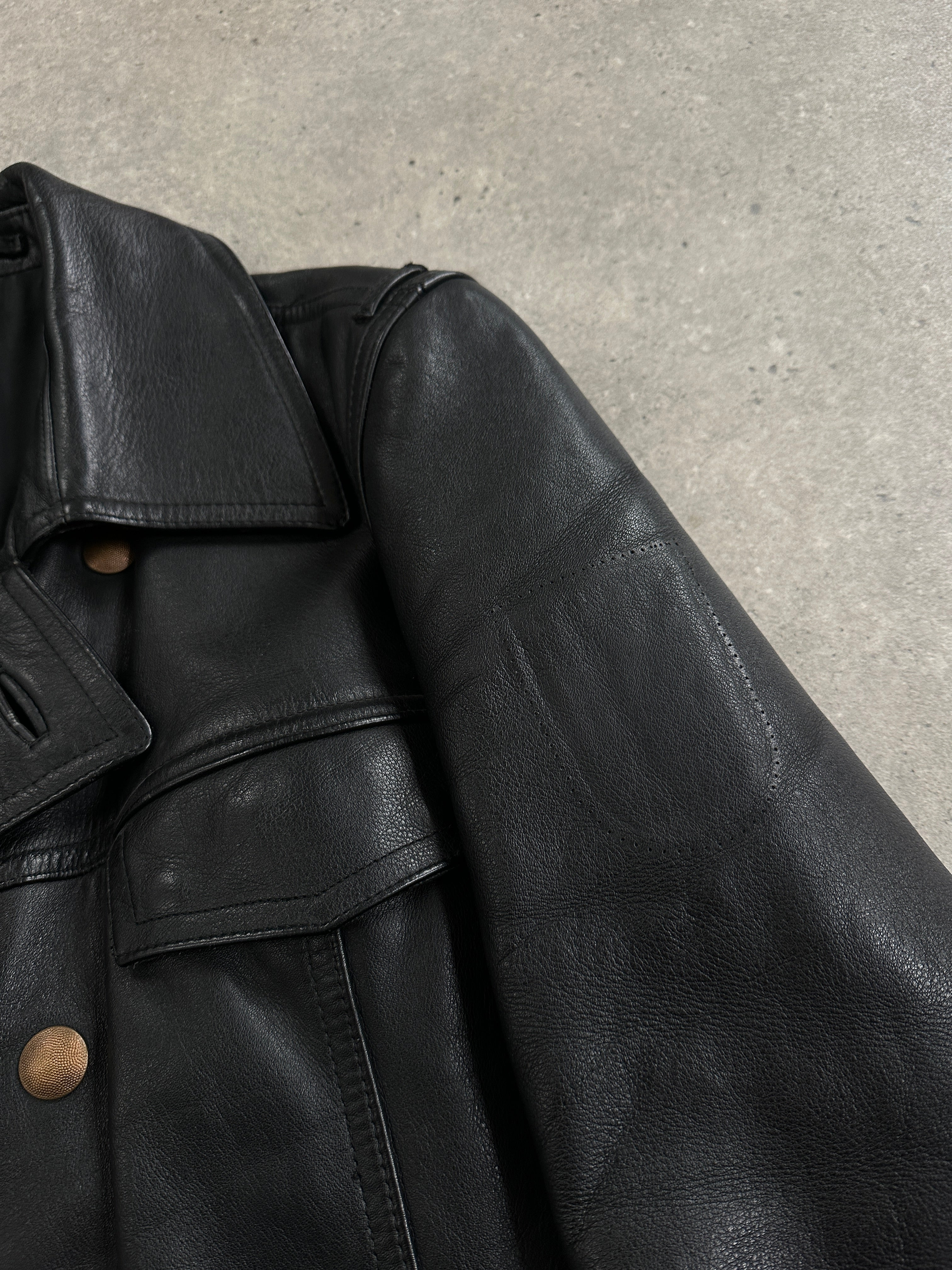 Vintage 1980s double-breasted military leather jacket in black, with epaulets and brass buttons, displayed on a hanger.