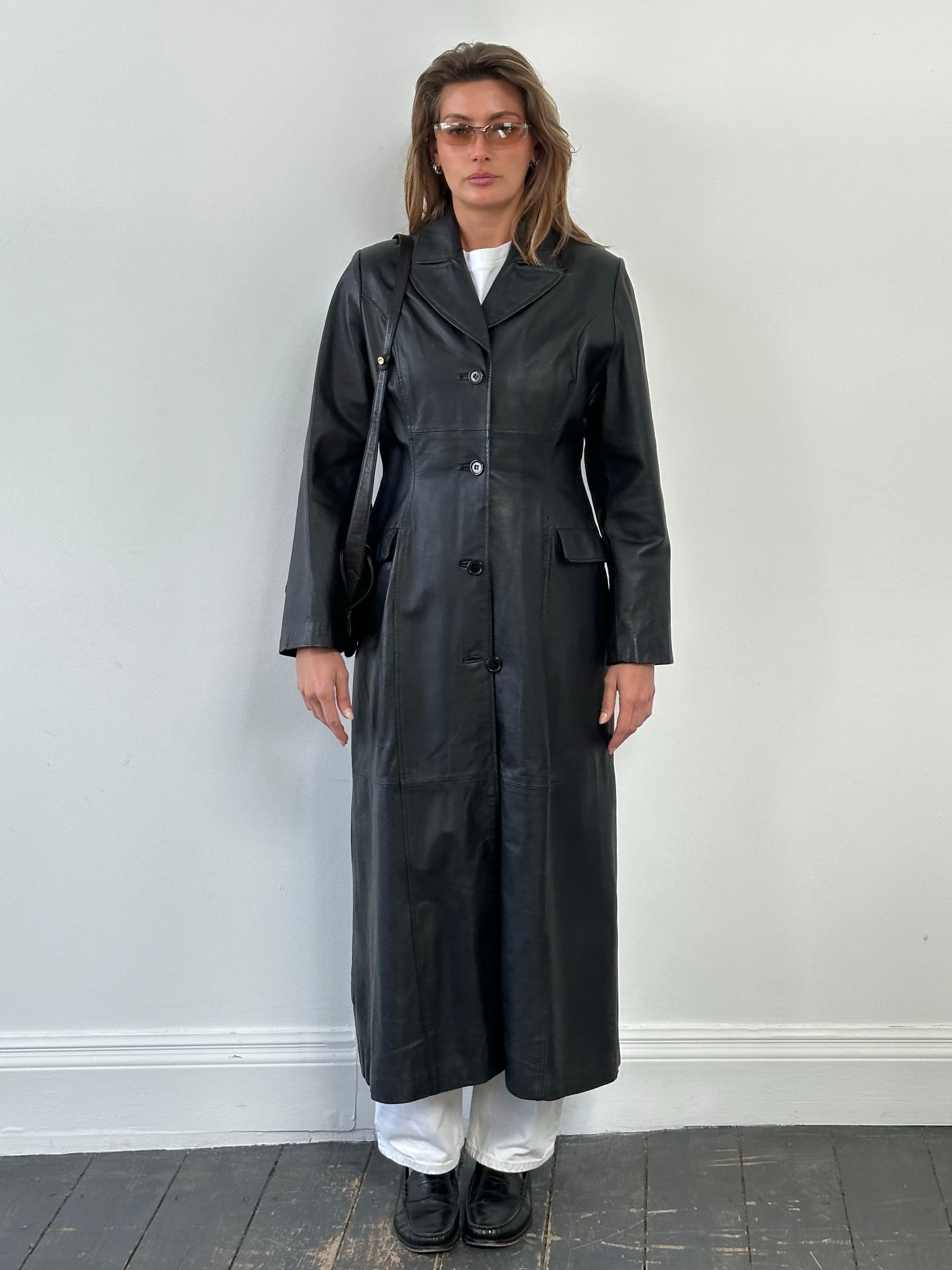 Vintage 1980s leather trench coat, floor-length design in size M, displayed on a hanger with detailed stitching and classic style.