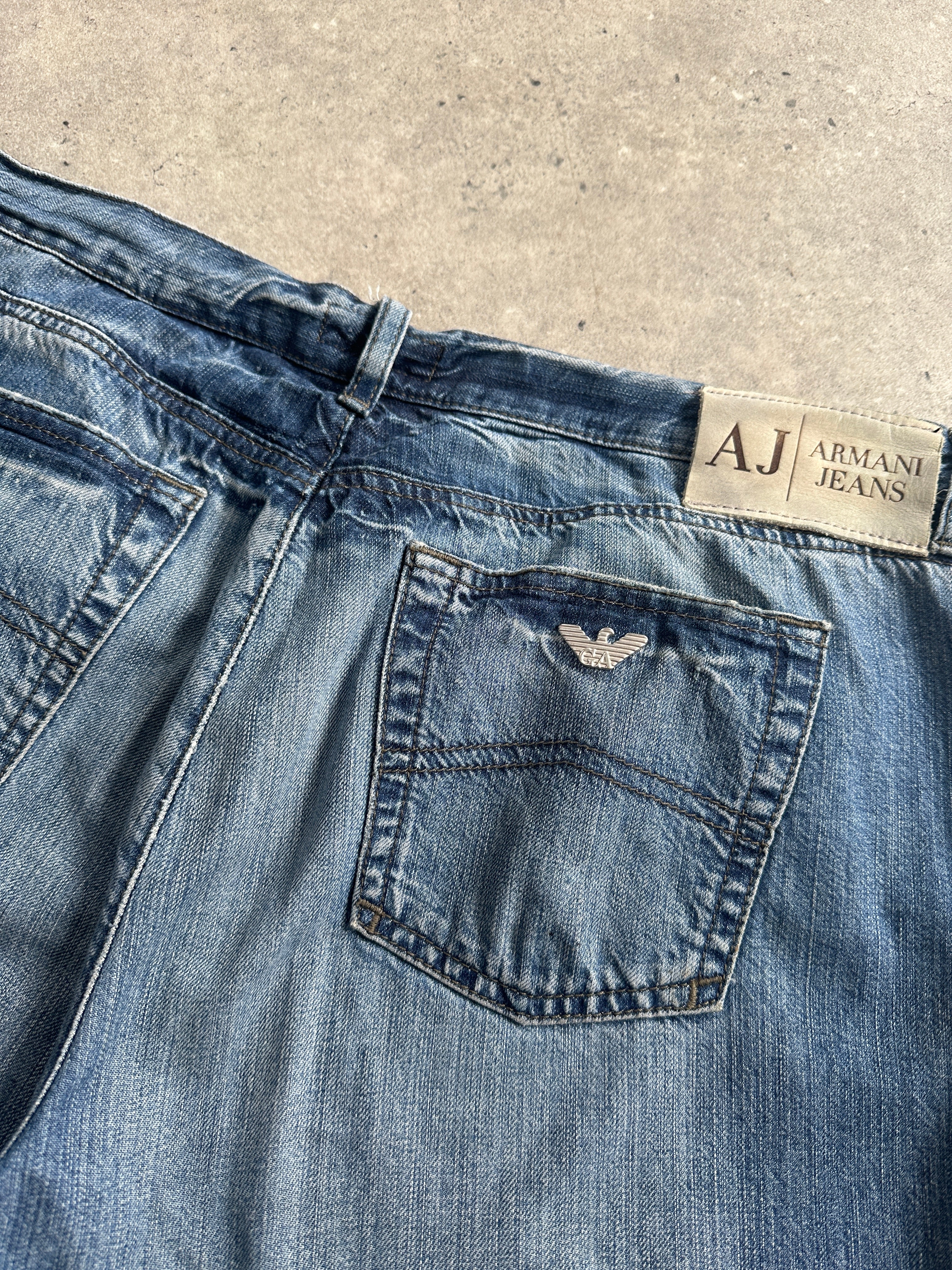Armani Jeans stonewashed mid-waist denim jeans in size W34, shown on a hanger with visible faded blue fabric and classic stitching.