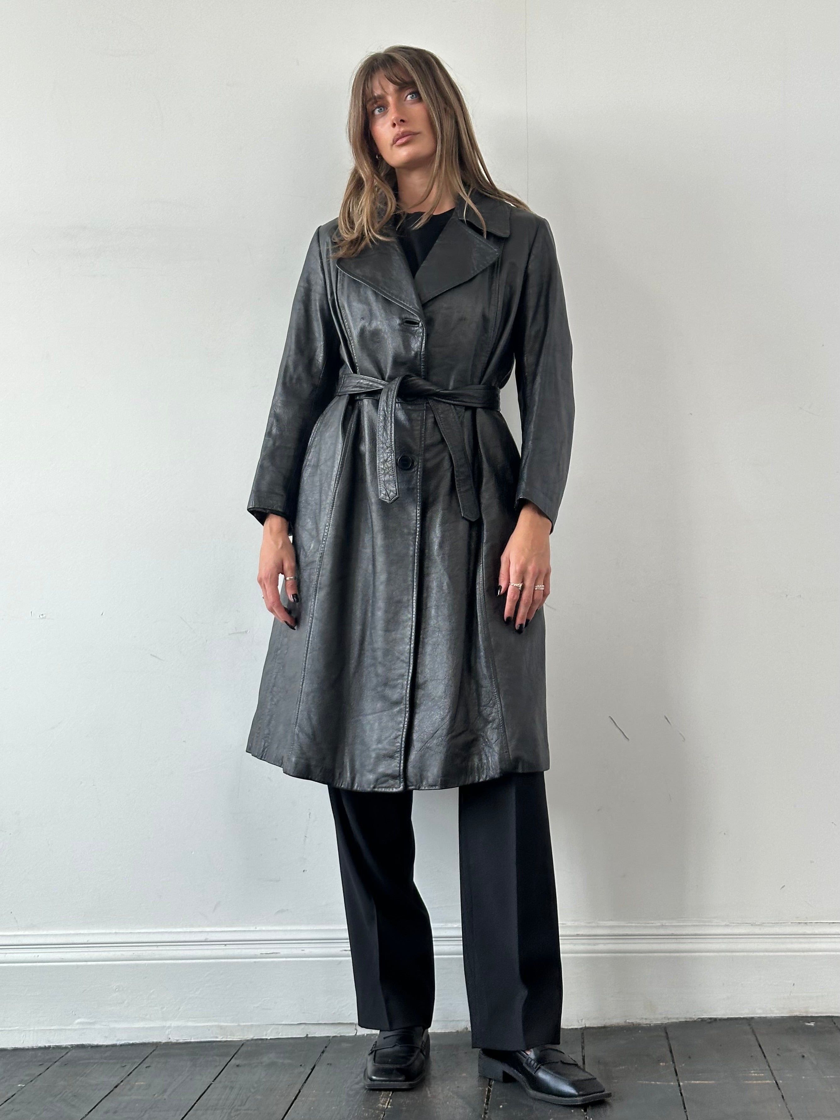 Vintage belted leather trench coat in black, stylish leather jacket with waist belt, classic design, shown on a hanger.