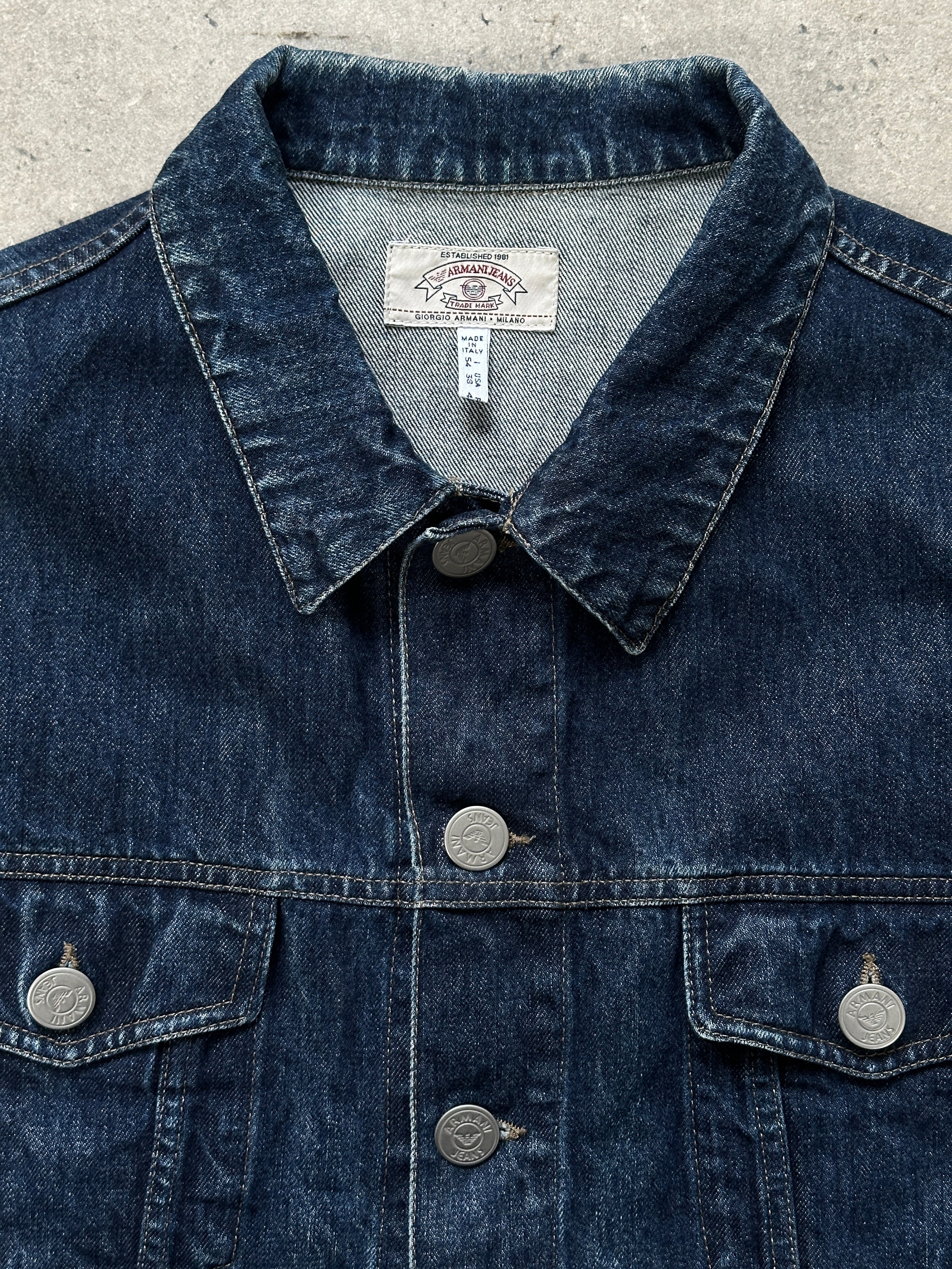 Armani Jeans 1900s mid wash denim jacket displayed on a hanger, showcasing classic style and detailed stitching.