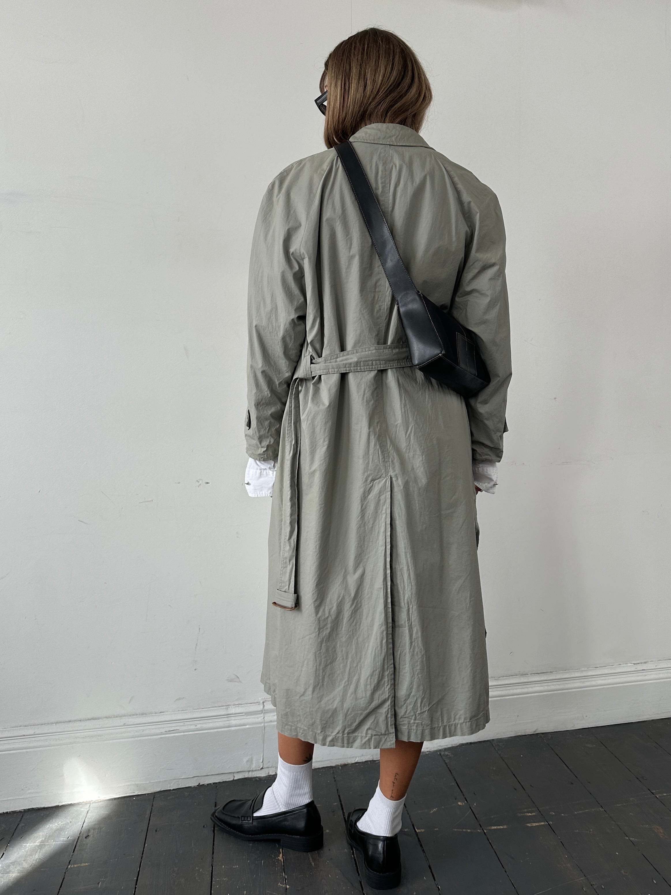 Christian Dior Le Connaisseur belted trench coat in camel color, shown on a model with classic design and double-breasted front.