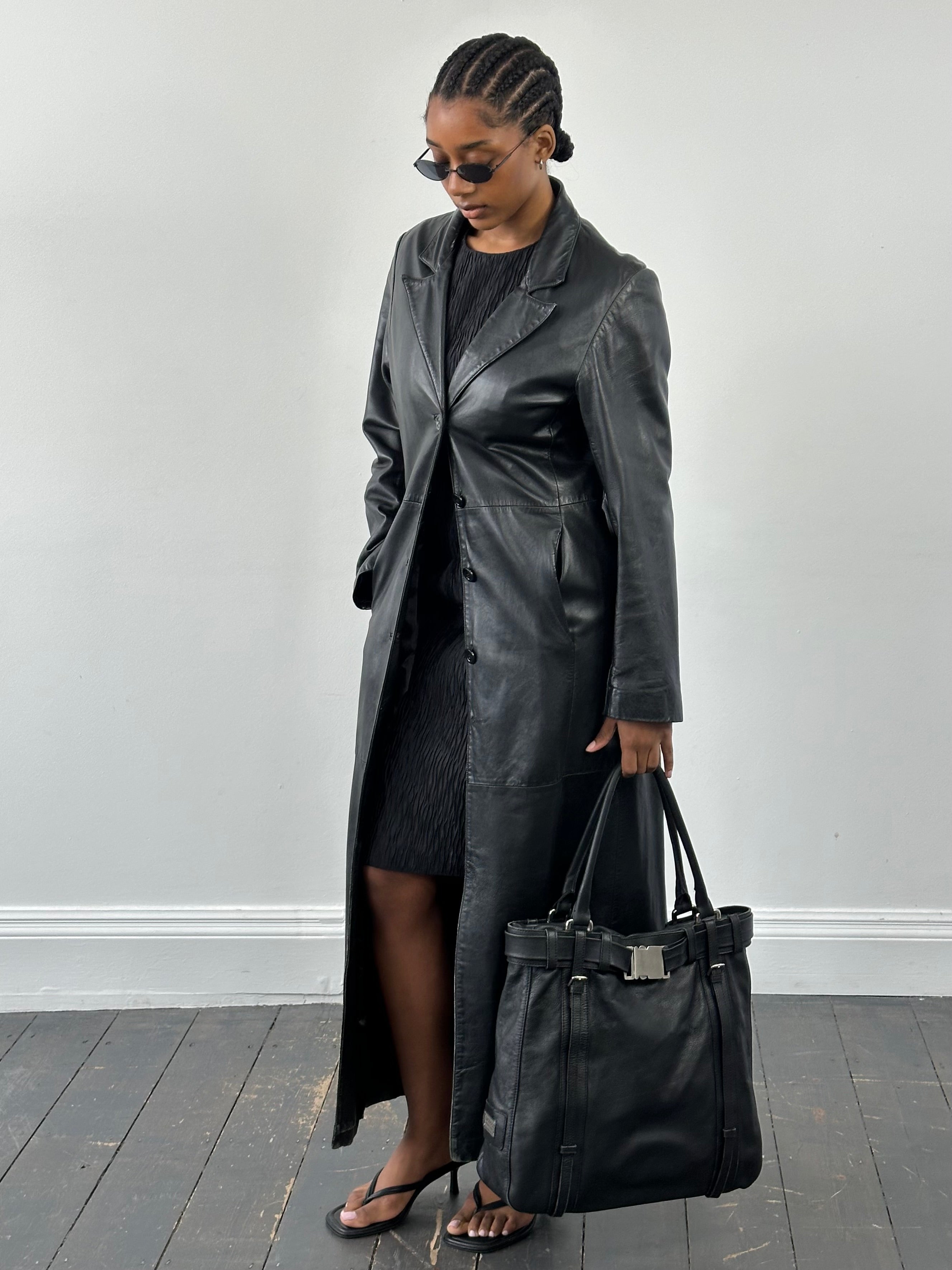 Vintage 1990s floor-length leather trench coat in black, displayed on a hanger with details of the classic vintage leather jacket style.